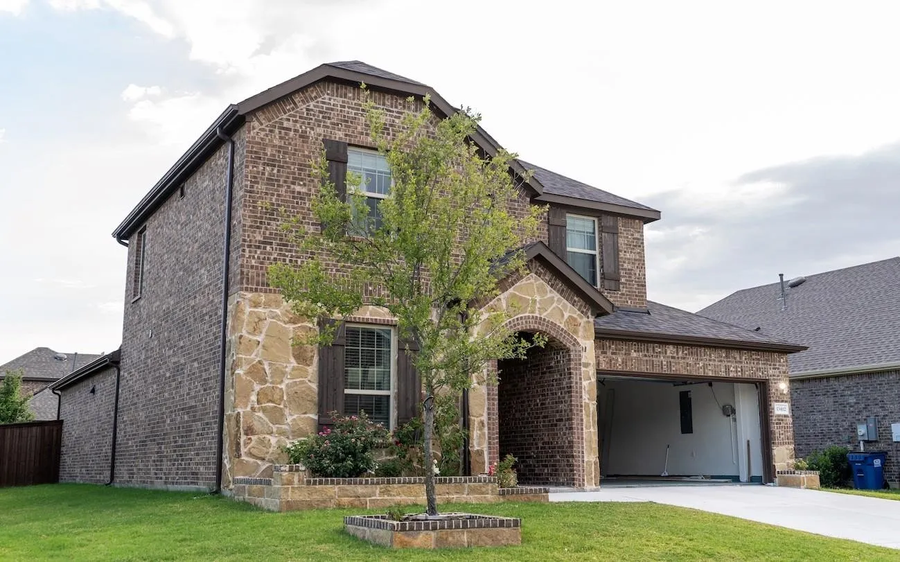 Two-story brick and stone exterior, arched entryway, attached garage, gabled roofline, and manicured landscaping