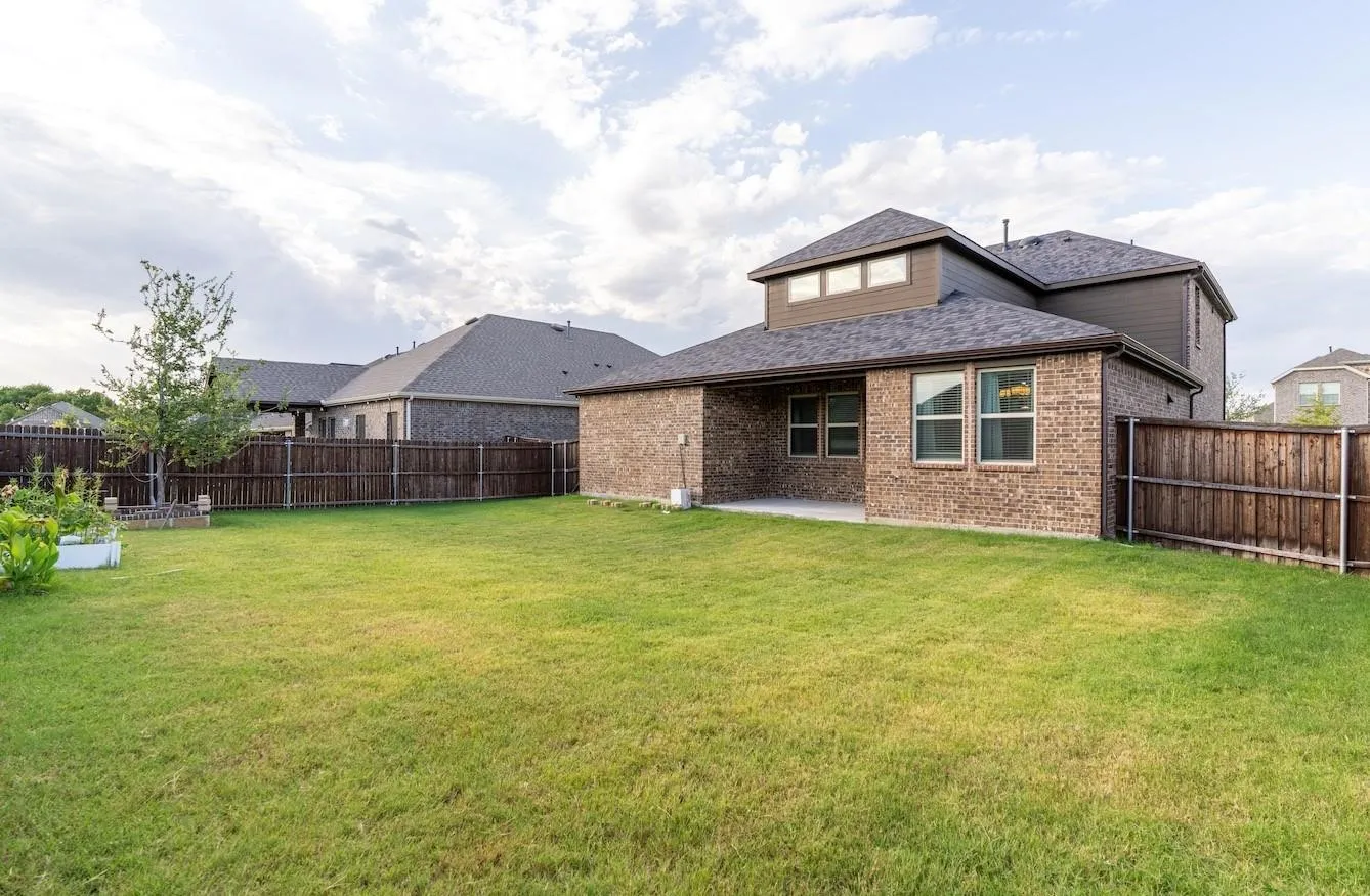 Expansive grassy yard with a privacy fence, brick exterior, and covered patio