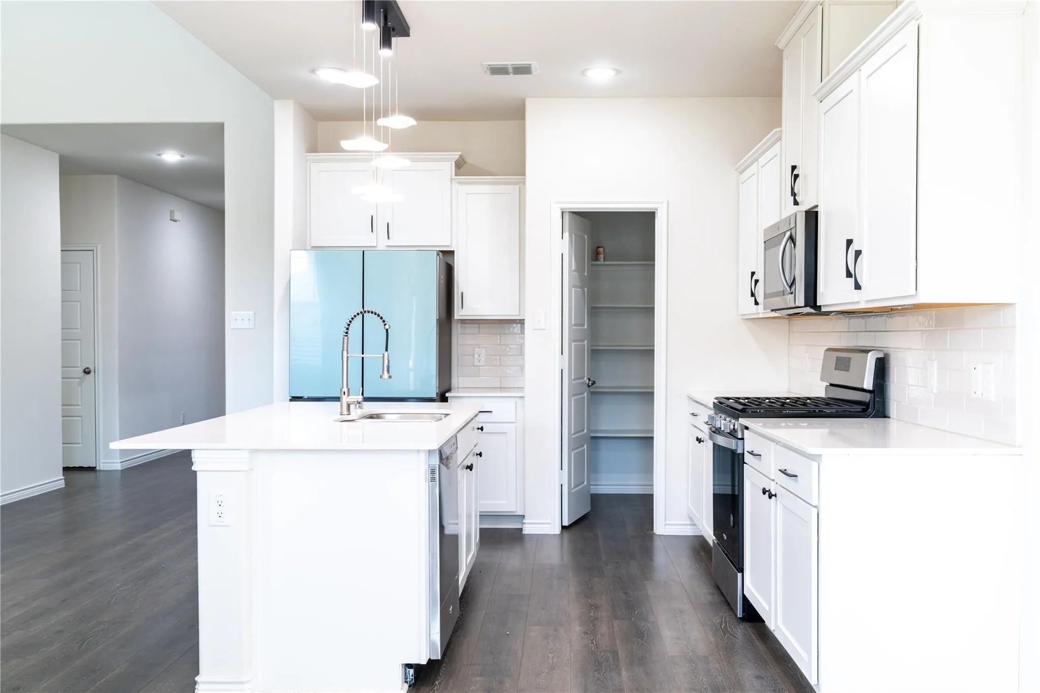 Kitchen featuring an expansive island with an integrated sink, white cabinetry, a built-in microwave, a gas range, and wood-finish flooring