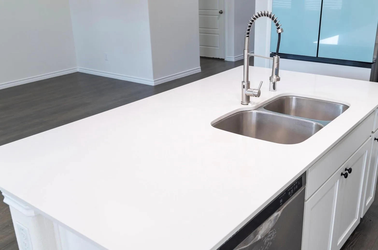 White solid surface countertop, double basin stainless steel sink, brushed nickel high-arc faucet, integrated dishwasher, white shaker-style cabinetry