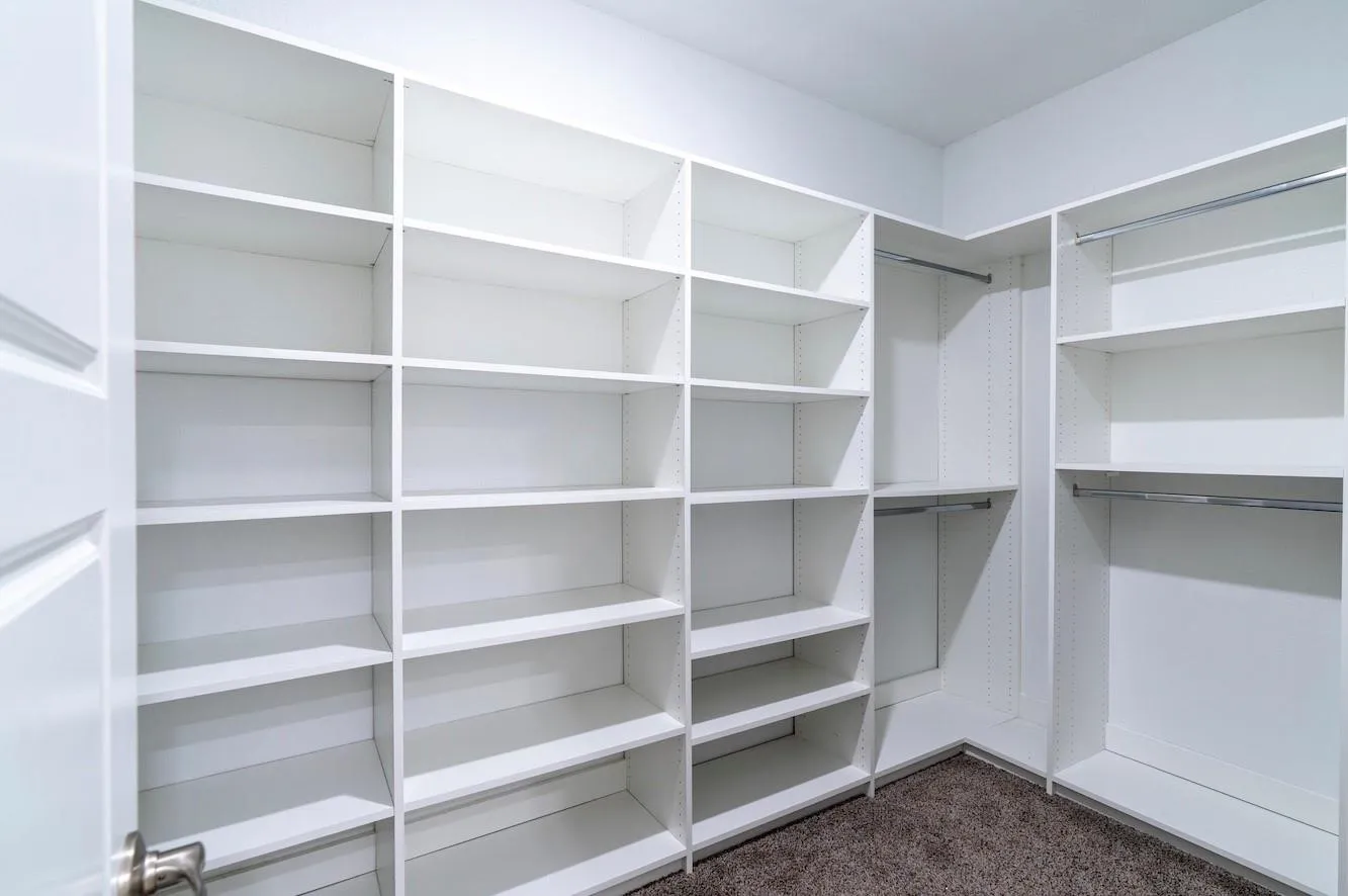 Custom closet system with white shelving, multiple hanging rods, and carpet flooring