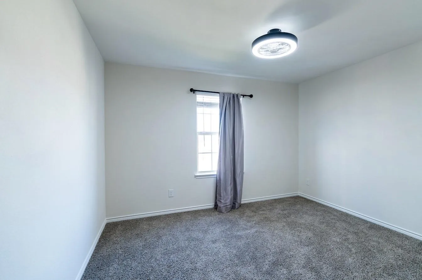 Neutral wall color, window with natural light, gray carpeting, and a flush-mount ceiling light fixture