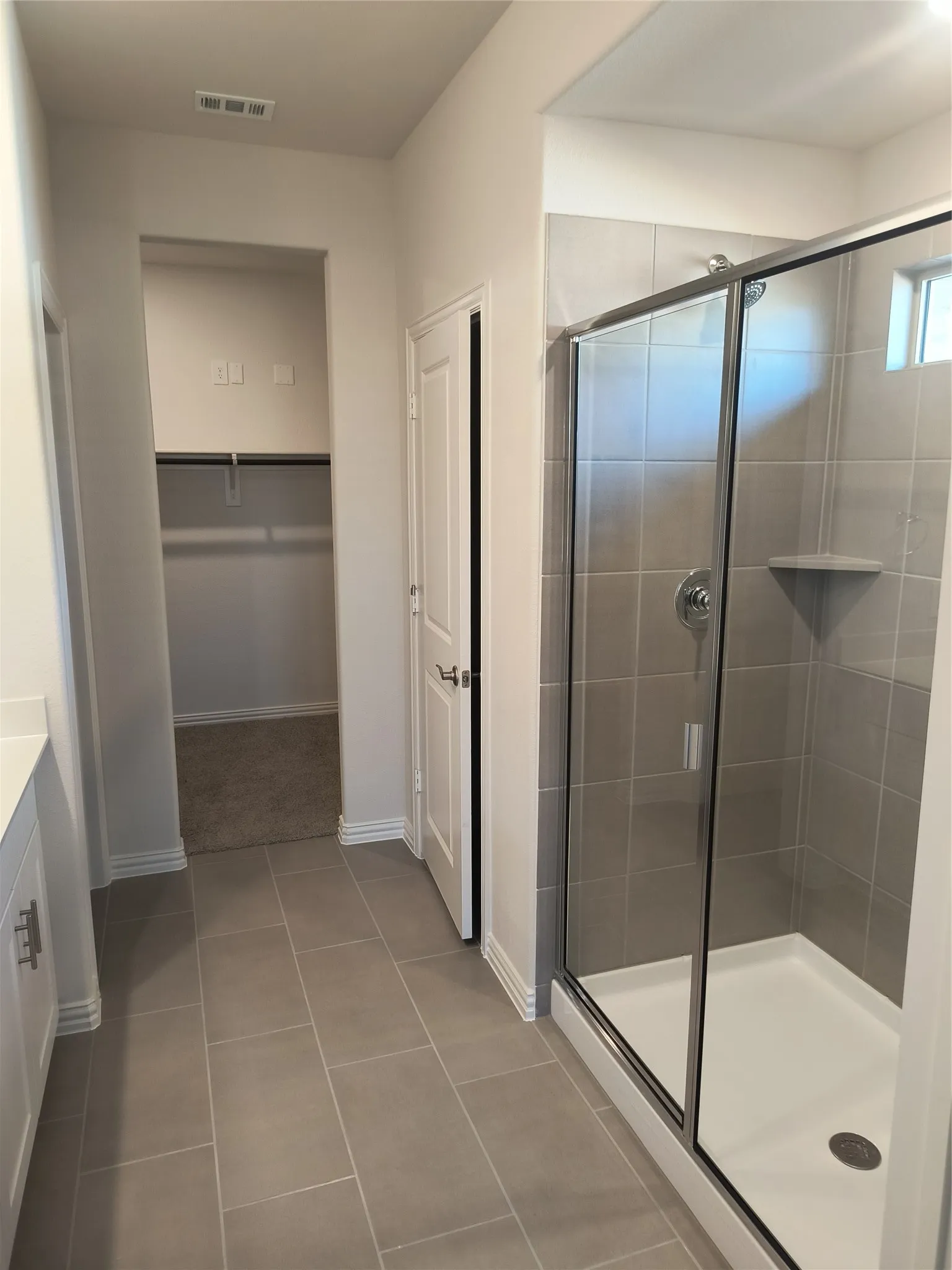 Spacious walk-in shower with glass enclosure, large format tile, and a built-in shelf