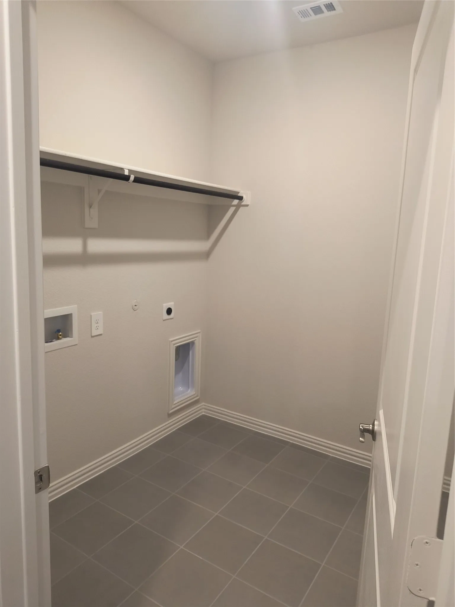 Utility room with tile flooring, wall-mounted shelving, and clothes rod