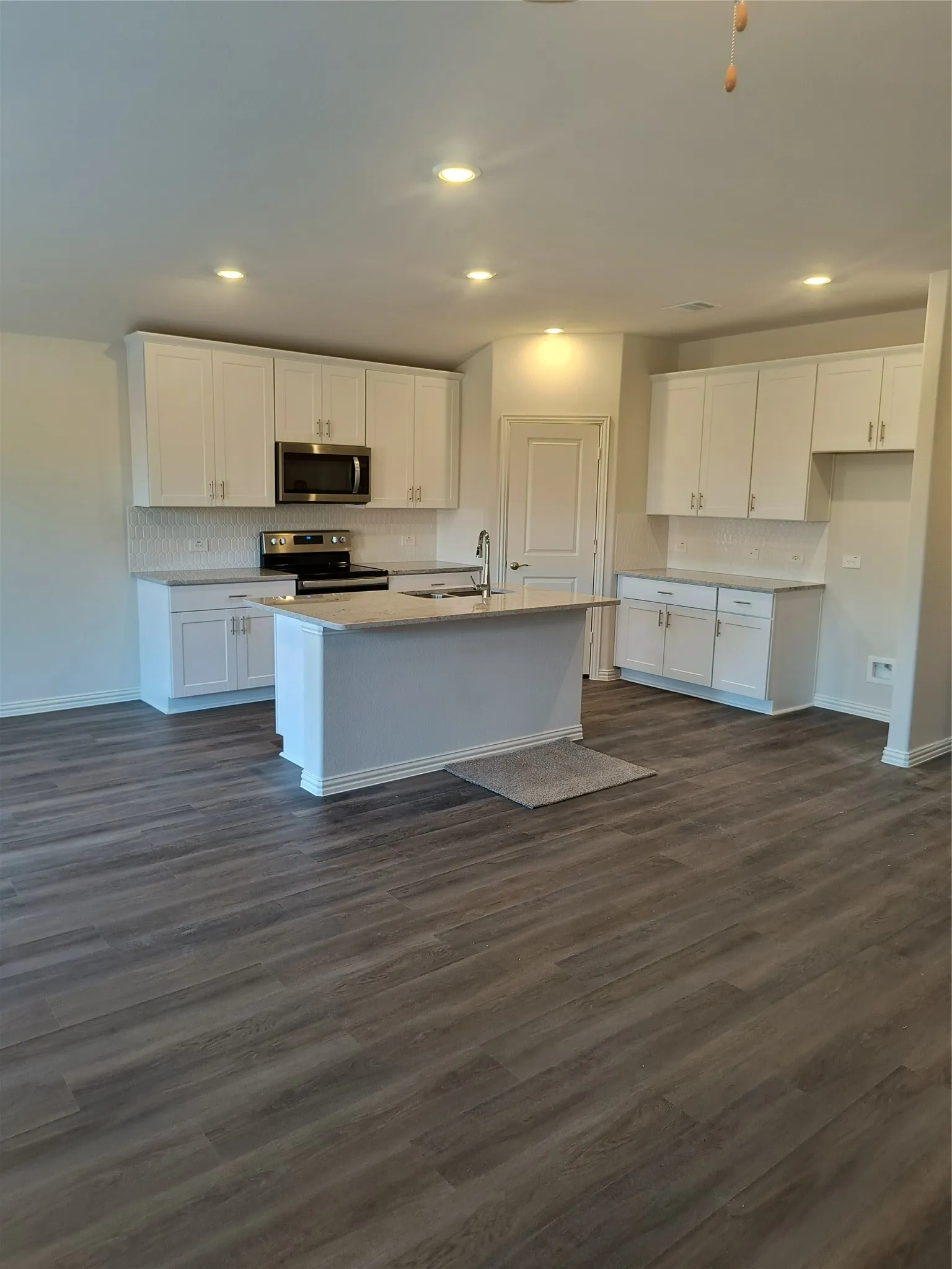 Modern kitchen featuring an island, stainless steel appliances, white cabinetry, and wood-finish flooring