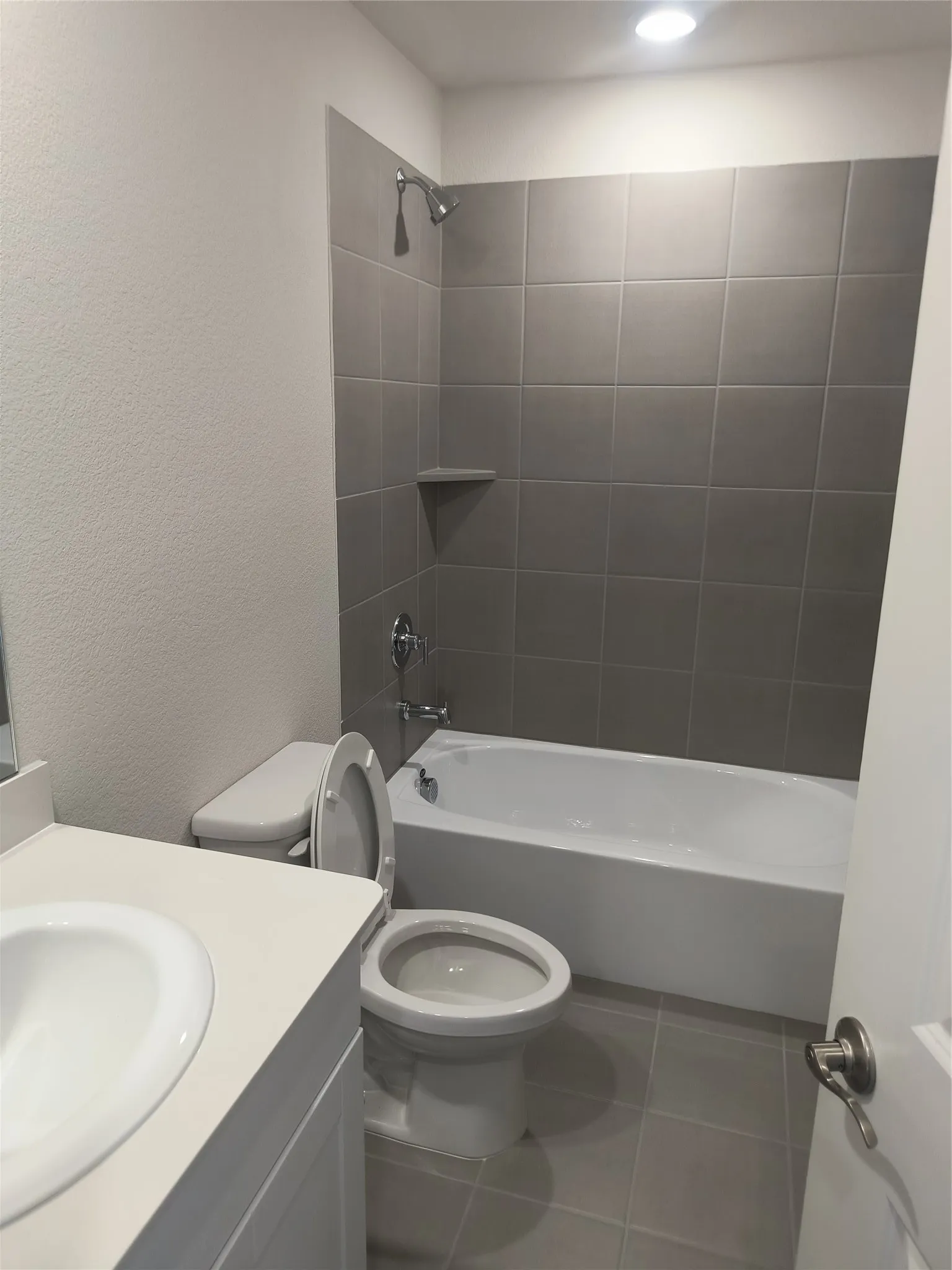 Bathroom featuring a white vanity with integrated sink, white toilet, tiled flooring, and a tub/shower combination with grey wall tiling