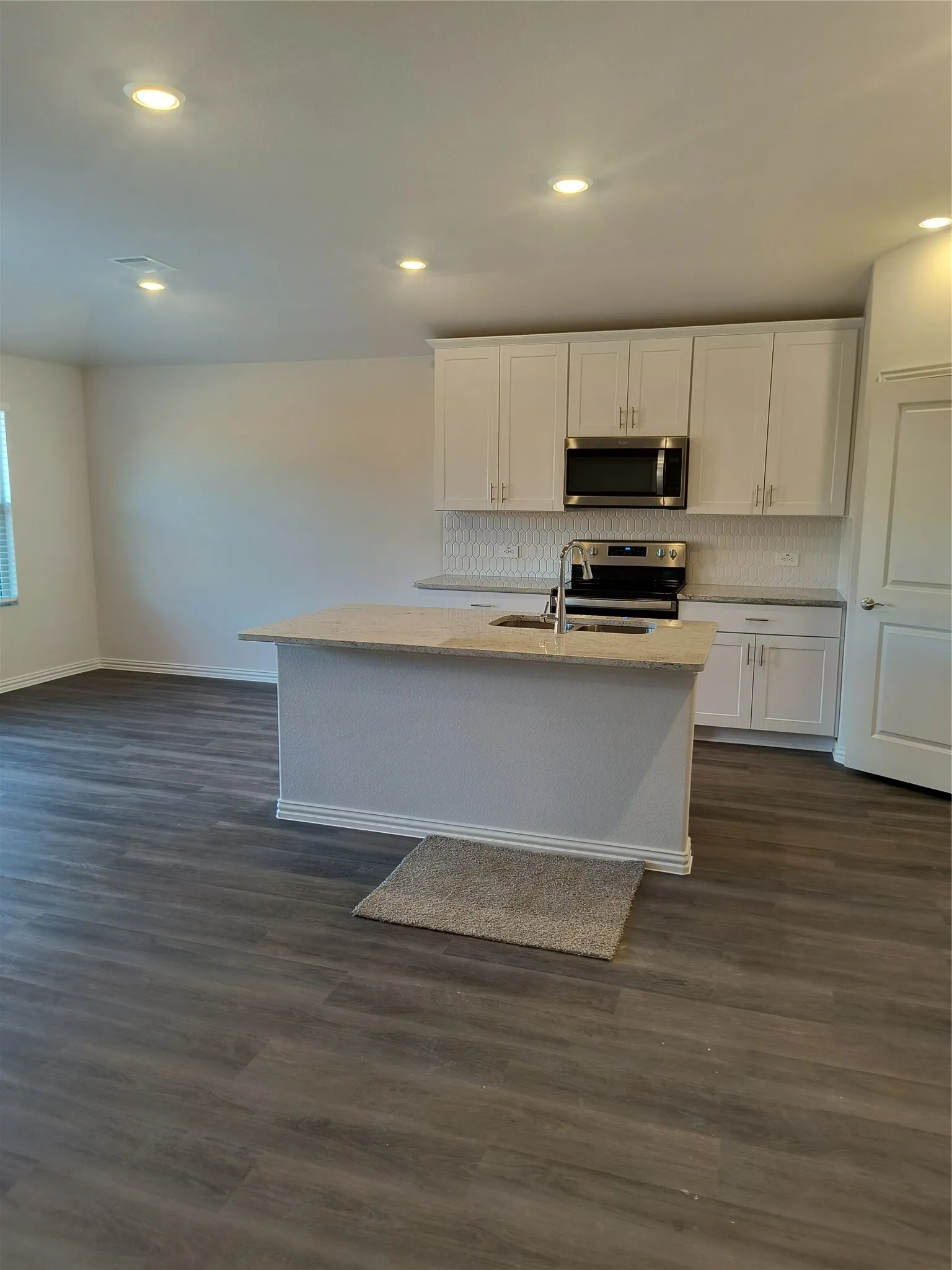 Modern kitchen featuring white shaker cabinetry, stainless steel appliances, a center island with sink, and wood-finish flooring