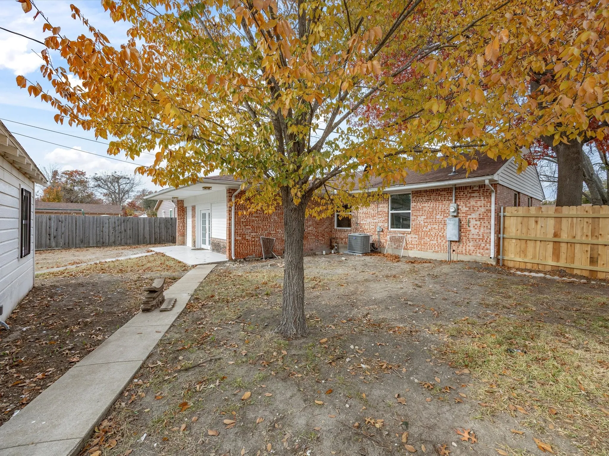 Spacious backyard featuring a concrete walkway, mature tree, and partial wood fencing