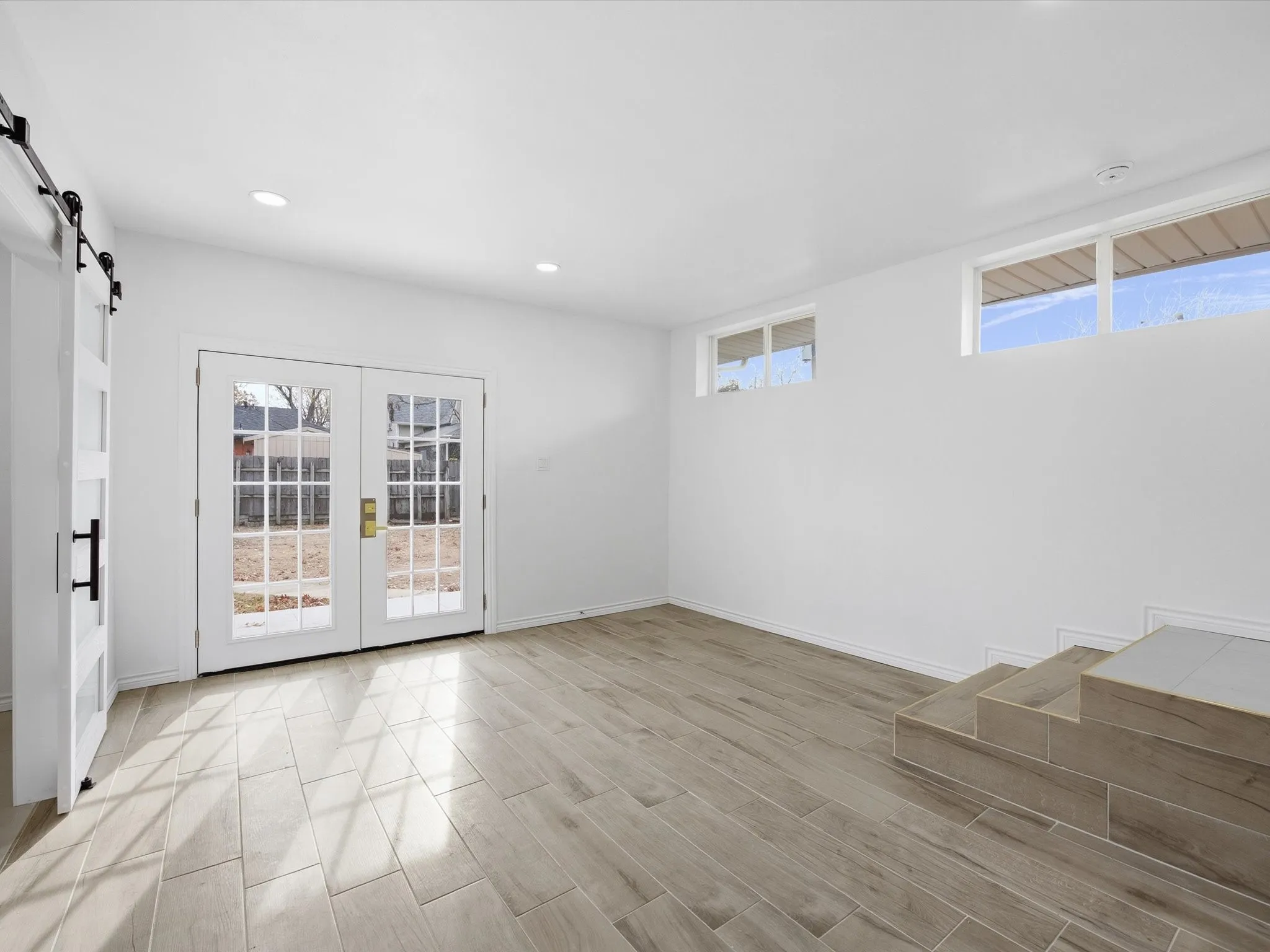 Recessed lighting, wood-finish tile flooring, white shaker-style barn door, French doors, and tiled steps