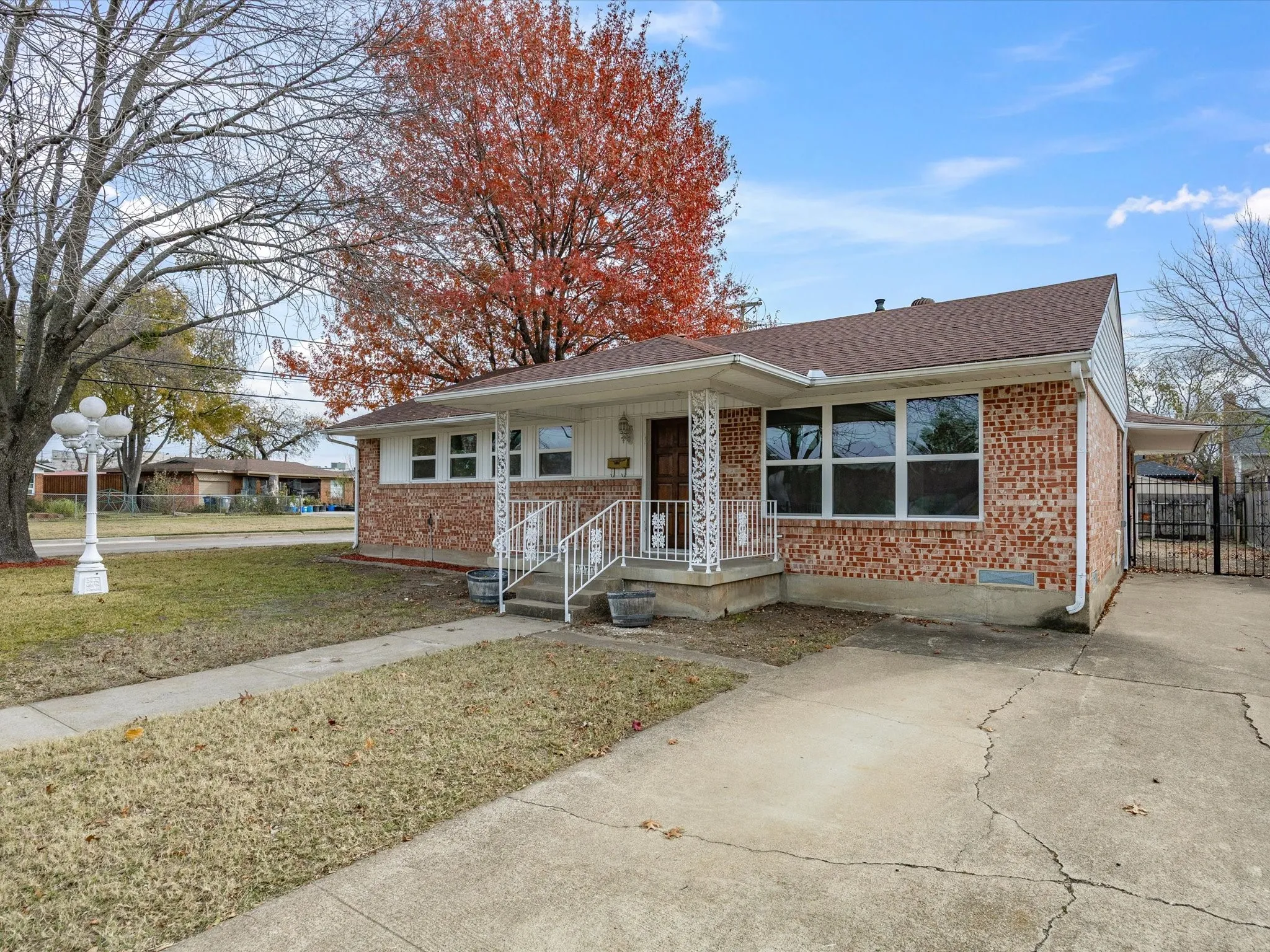 Brick exterior featuring a covered front porch with decorative railings, multiple front-facing windows, and a paved driveway leading to a gated side entrance