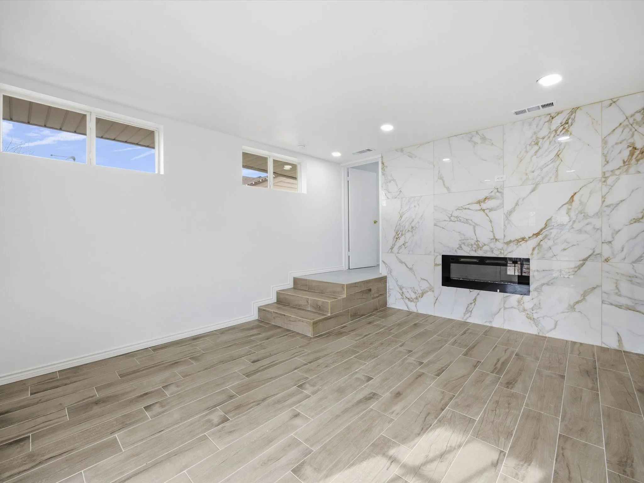 Porcelain tile flooring, recessed ceiling lighting, two windows, two-step platform, and a wall-mounted fireplace