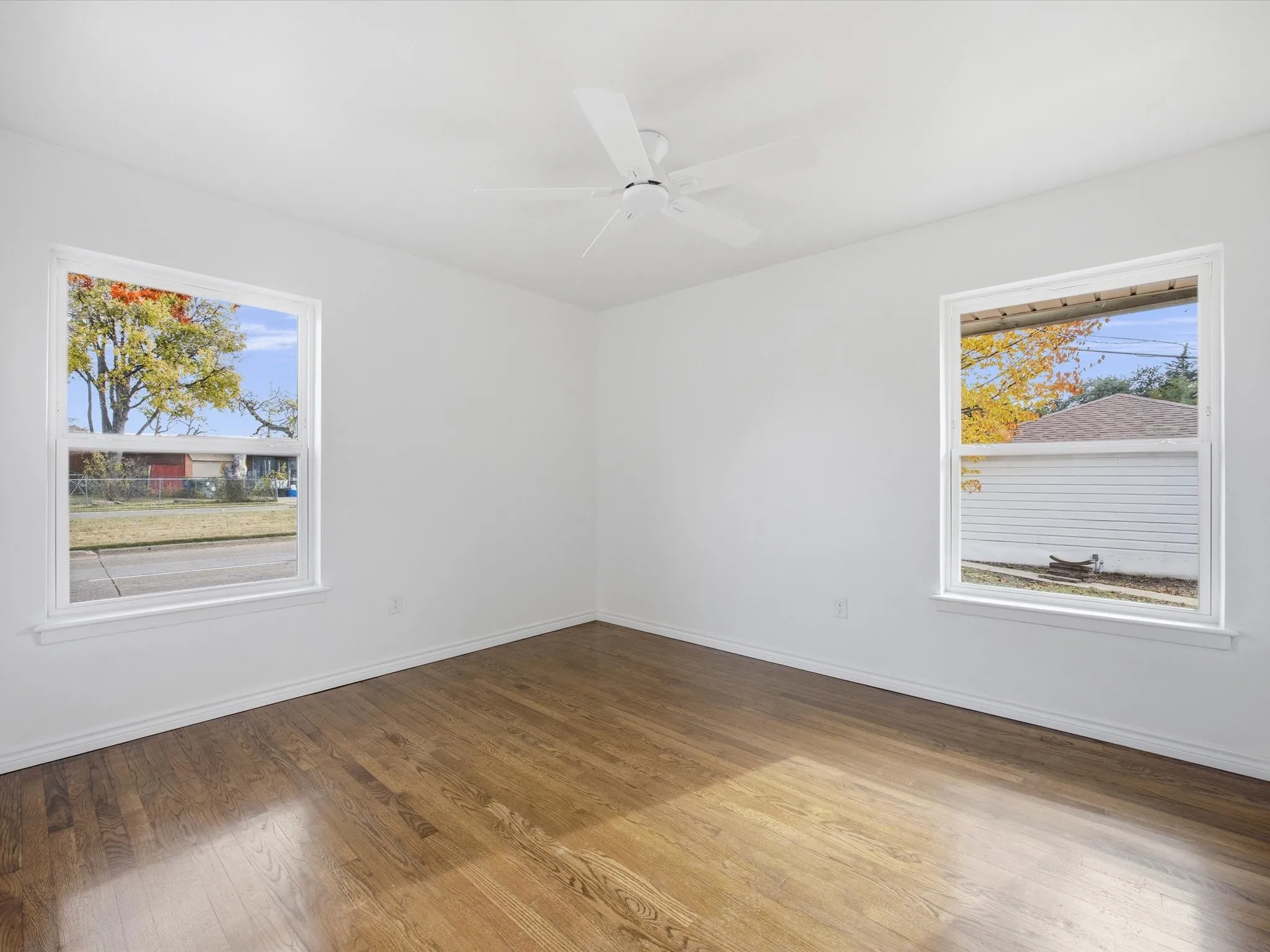 Wood-finish flooring, white walls, two windows with white trim, and a ceiling fan