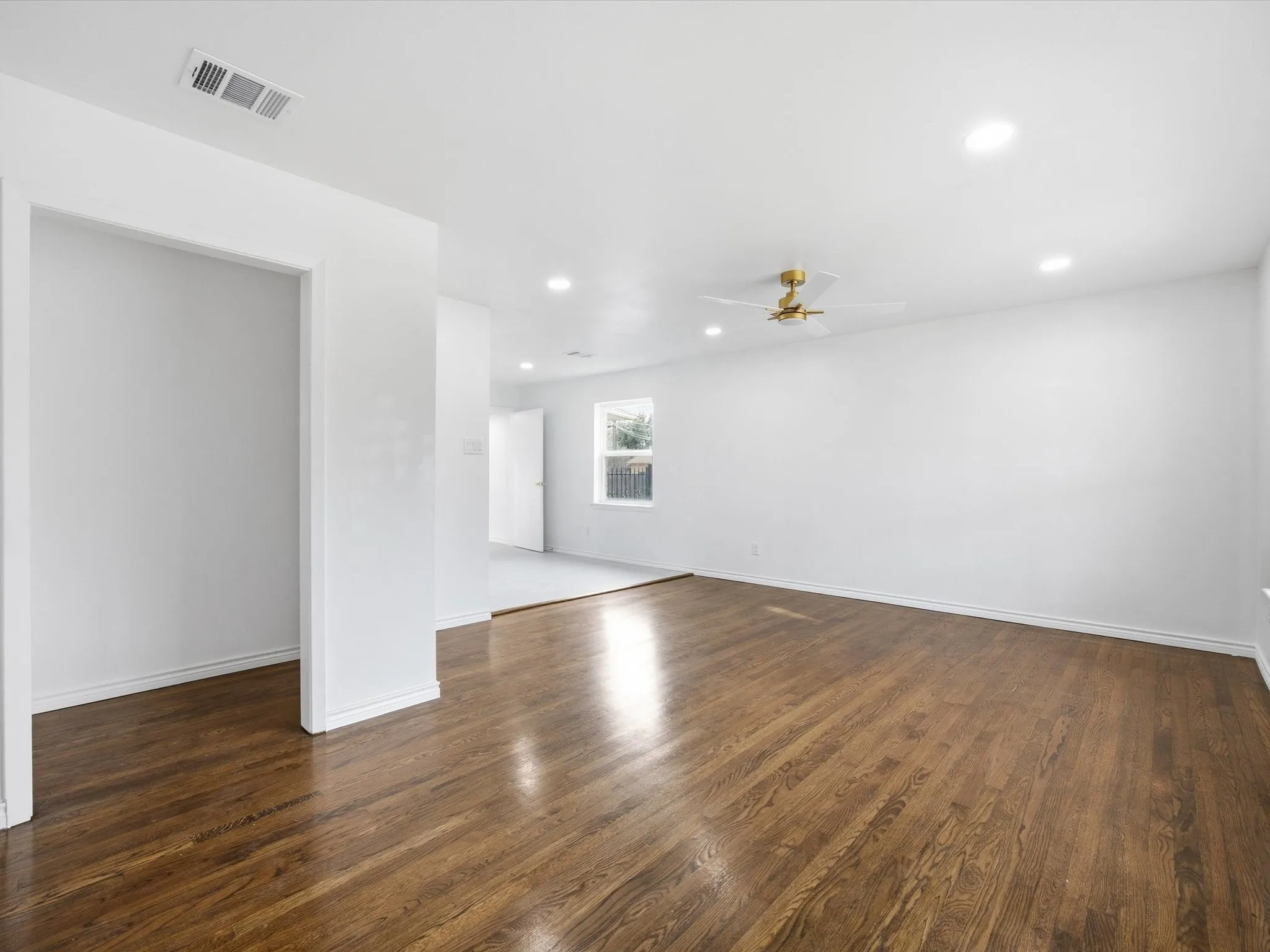 Wood-finish flooring, recessed lighting, ceiling fan with gold-tone accents, and white wall finishes