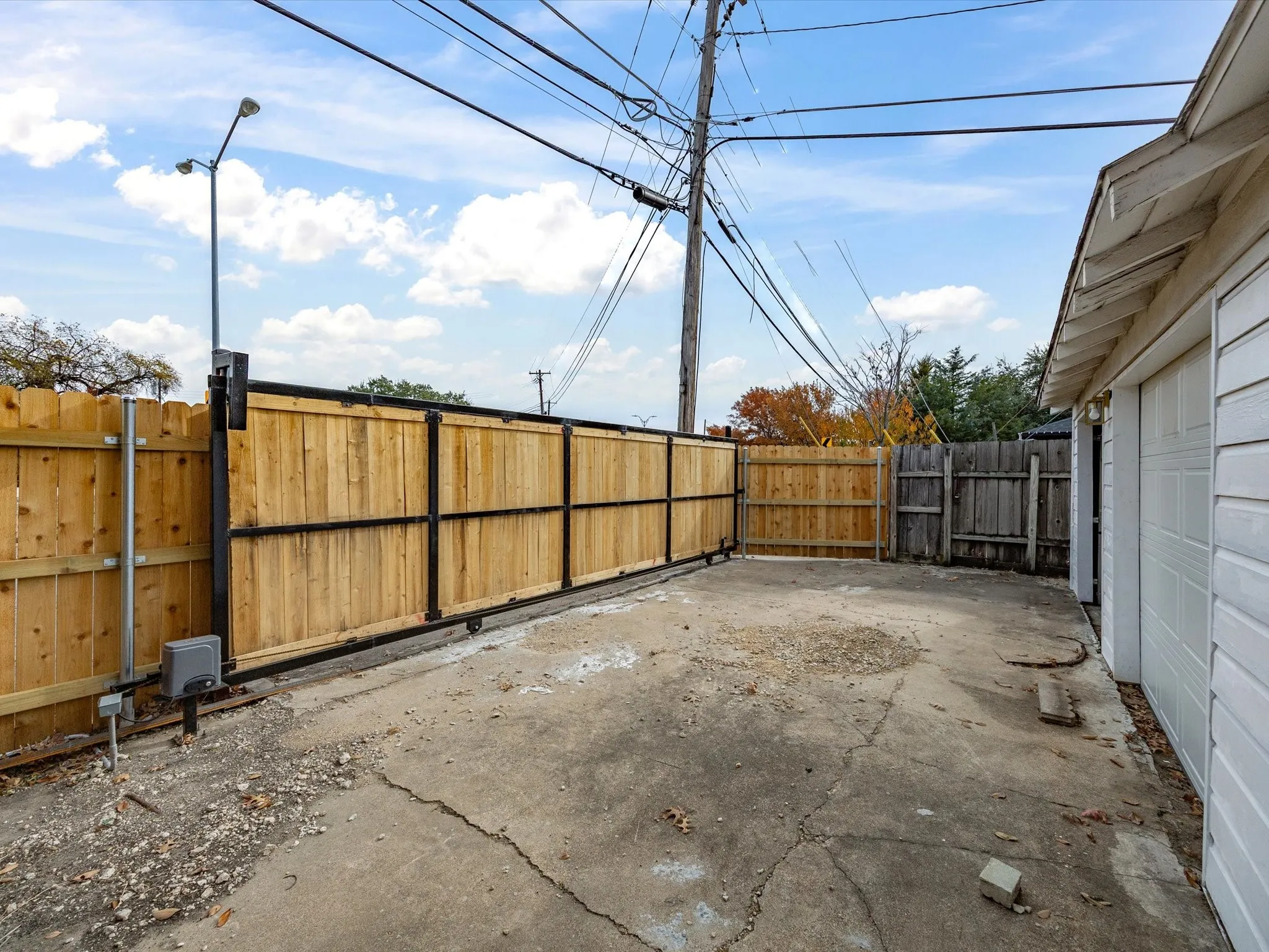 Paved outdoor area with a sliding wood-panel fence, integrated gate operator, and exterior lighting fixture