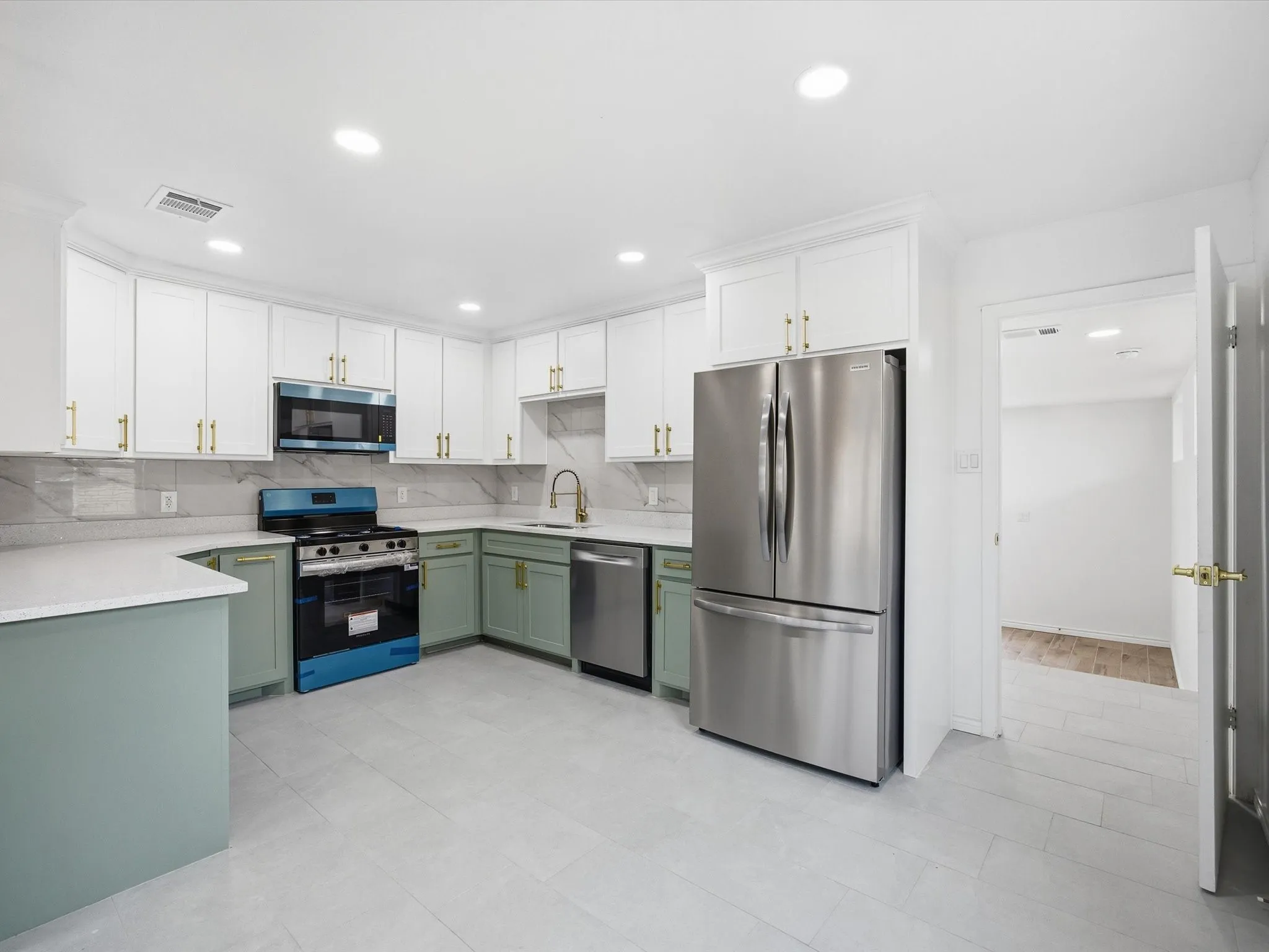 Kitchen featuring white upper cabinetry, sage green lower cabinetry, stainless steel appliances, light-toned countertops, and a tiled backsplash