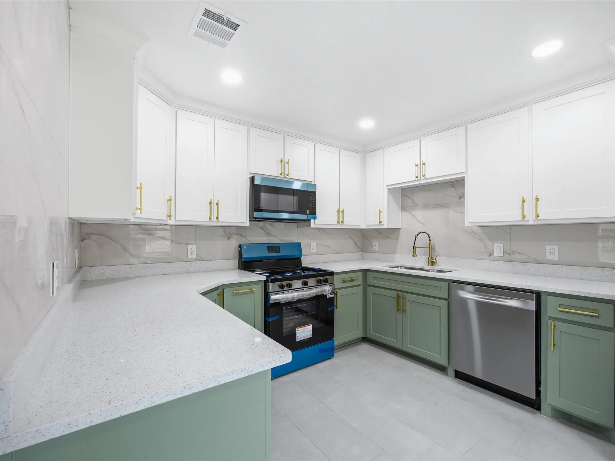 White upper cabinetry complemented by sage green lower cabinetry, light-colored countertops, a tile backsplash, and stainless steel appliances