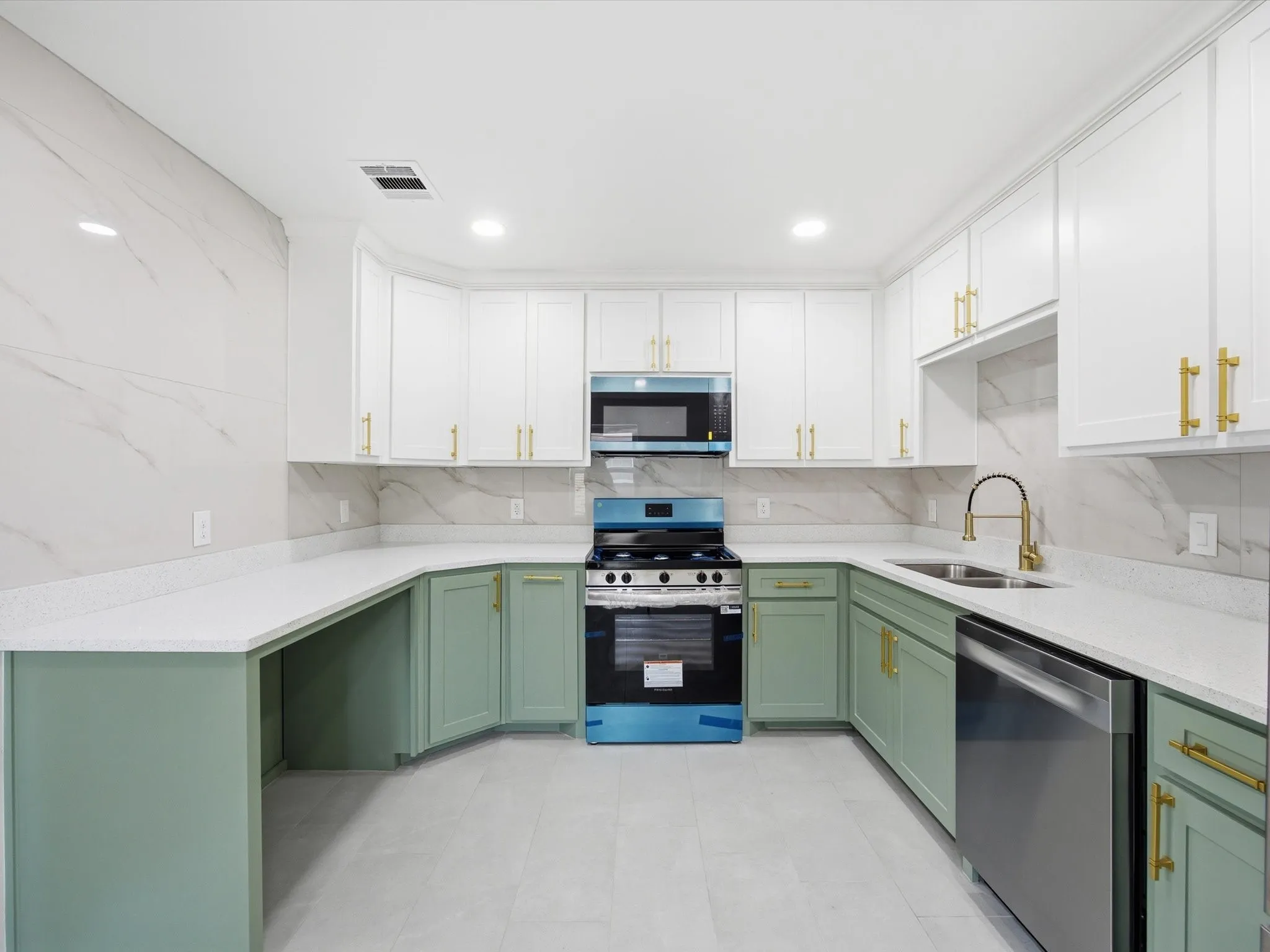 White shaker cabinetry with gold-finish hardware, stainless steel appliances, light-toned countertops, and two-tone lower cabinetry