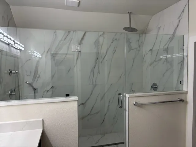 Huge walk-in shower with clear glass enclosure, marble-look tile walls, a rainfall showerhead, shower sprayer, and chrome fixtures