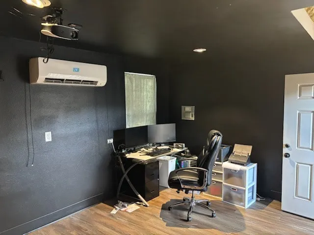 Outside office building with dark wall tones, featuring a wall-mounted mini-split AC unit, recessed ceiling lighting, and a paneled interior door
