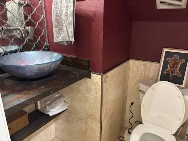 Vessel sink with a wood-finish vanity, decorative wall-mounted faucet, and arabesque mirror