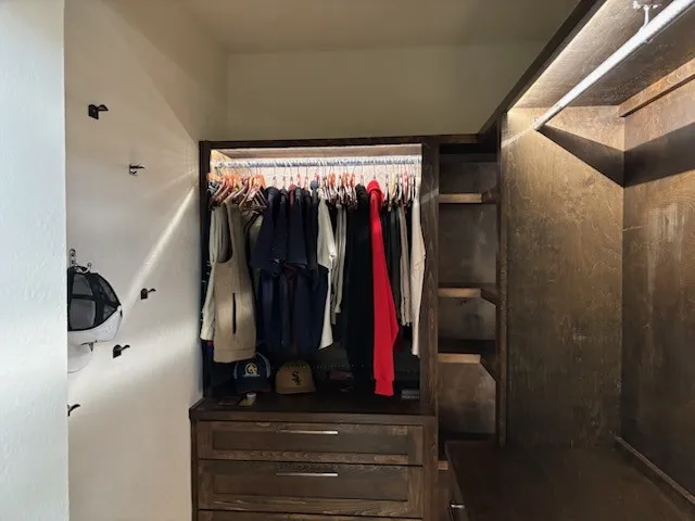 Built-in custom primary closet system featuring stained wood-finish cabinetry, integrated shelving, and illuminated hanging rods