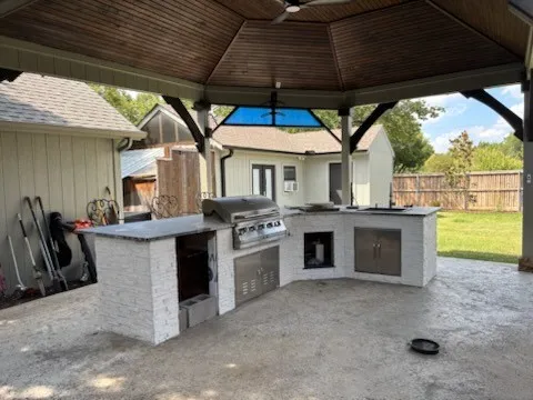 Expansive outdoor kitchen featuring a built-in grill, stainless steel cabinetry, and stone-finish countertops under a covered patio with a wood-finish custom ceiling