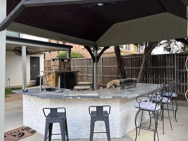 Covered outdoor kitchen featuring a built-in stone fireplace, integrated sink, and an expansive countertop for all your outdoor entertaining needs