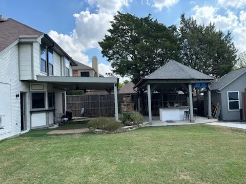 Expansive backyard featuring a covered patio, detached gazebo with built-in bar, manicured lawn, and mature trees