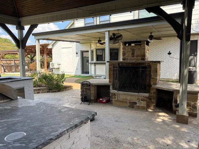 Expansive covered patio featuring a stone-clad outdoor fireplace, built-in outdoor kitchen with stone countertop, and wood-finish ceiling with integrated fans