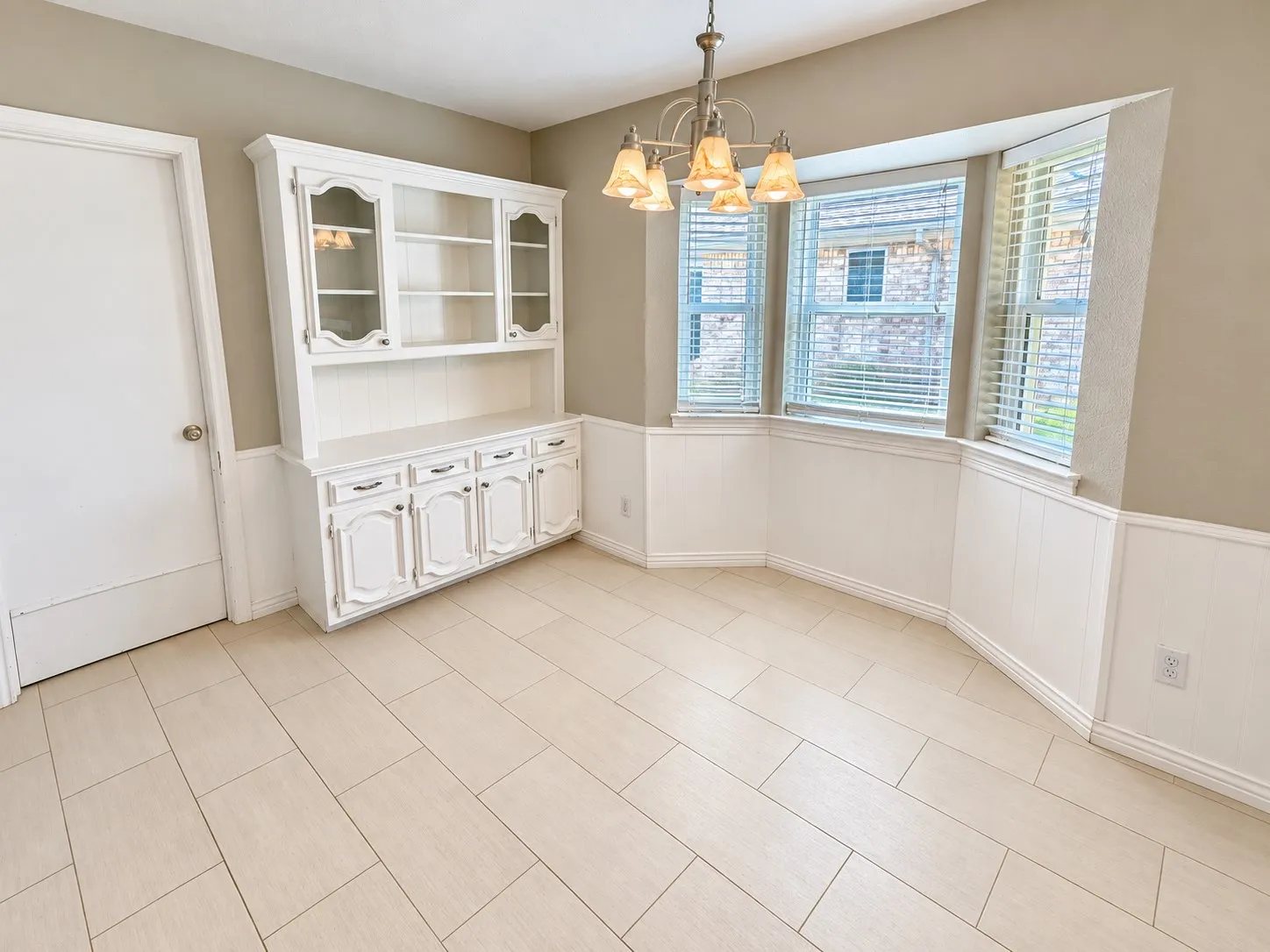 Recessed bay window with blinds, built-in display cabinetry, wainscoting, and wood-finish flooring