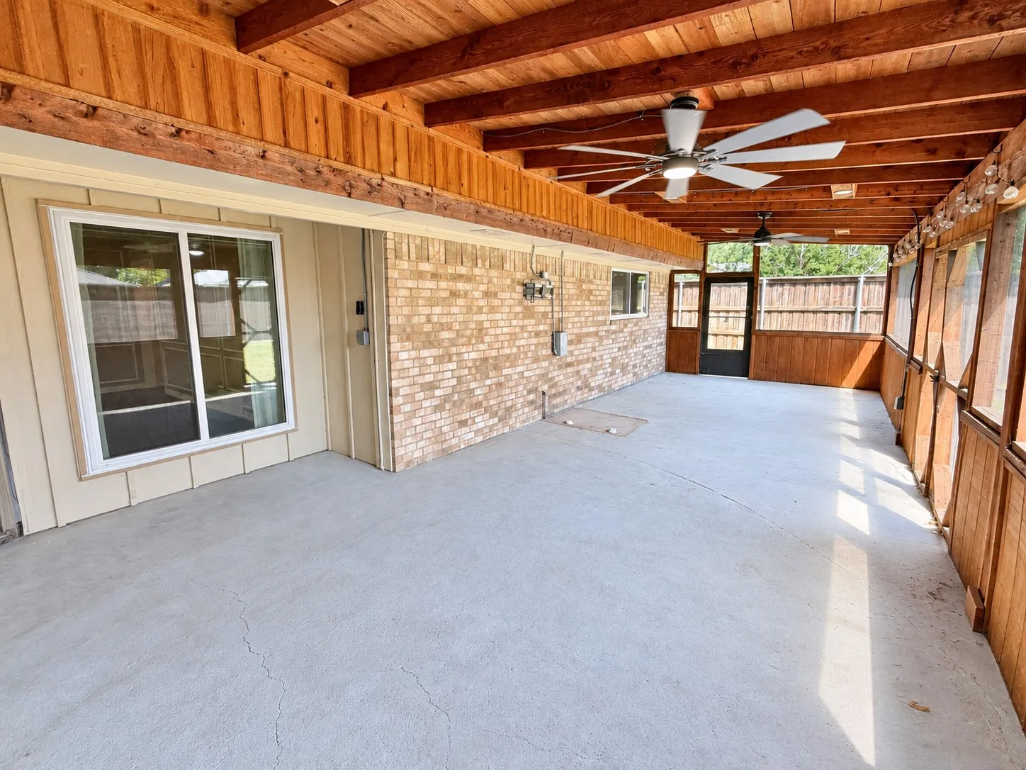 Expansive covered patio featuring a concrete floor, wood-plank ceiling, exposed wood beams, and multiple ceiling fans