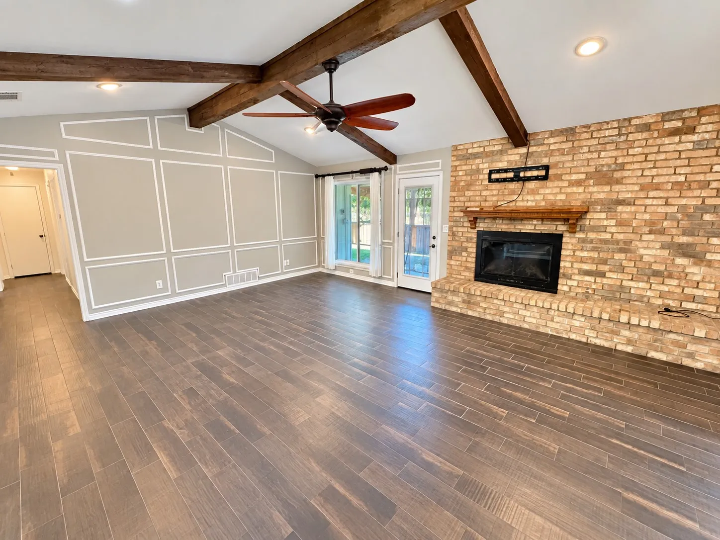 Vaulted ceiling with exposed wood beams, brick fireplace with wood mantel, wood-finish flooring, recessed lighting, and wall trim detailing