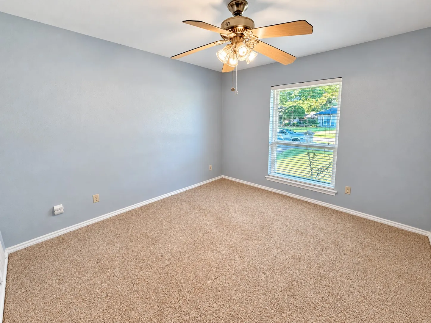 Carpeted flooring, light blue wall paint, window with blinds, white trim, and a ceiling fan with integrated lighting
