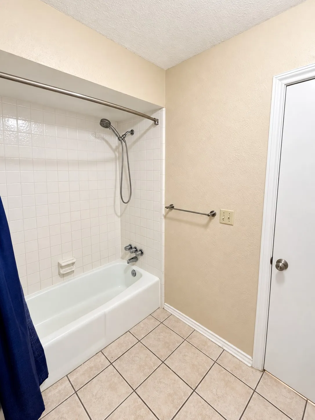 White bathtub with a chrome shower fixture, set against white square wall tiles