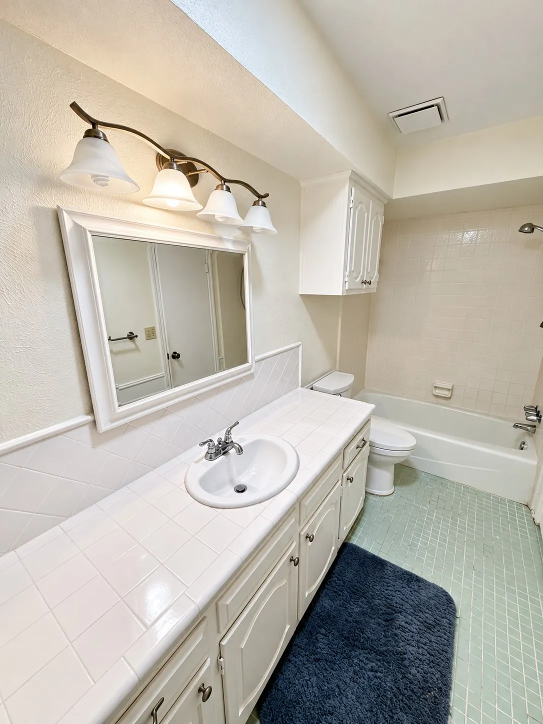 Extended vanity with an integrated sink, ample lower cabinetry, and a wall-mounted light fixture above a framed mirror