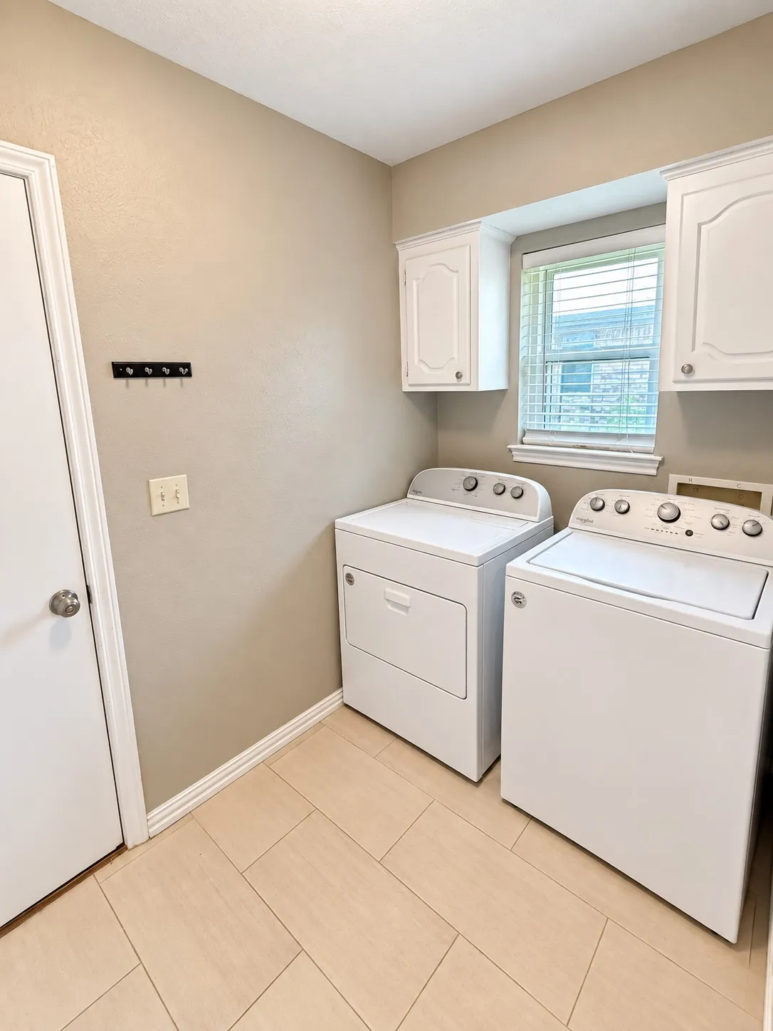 Laundry area featuring light-toned tile flooring, upper cabinetry, and a window with blinds