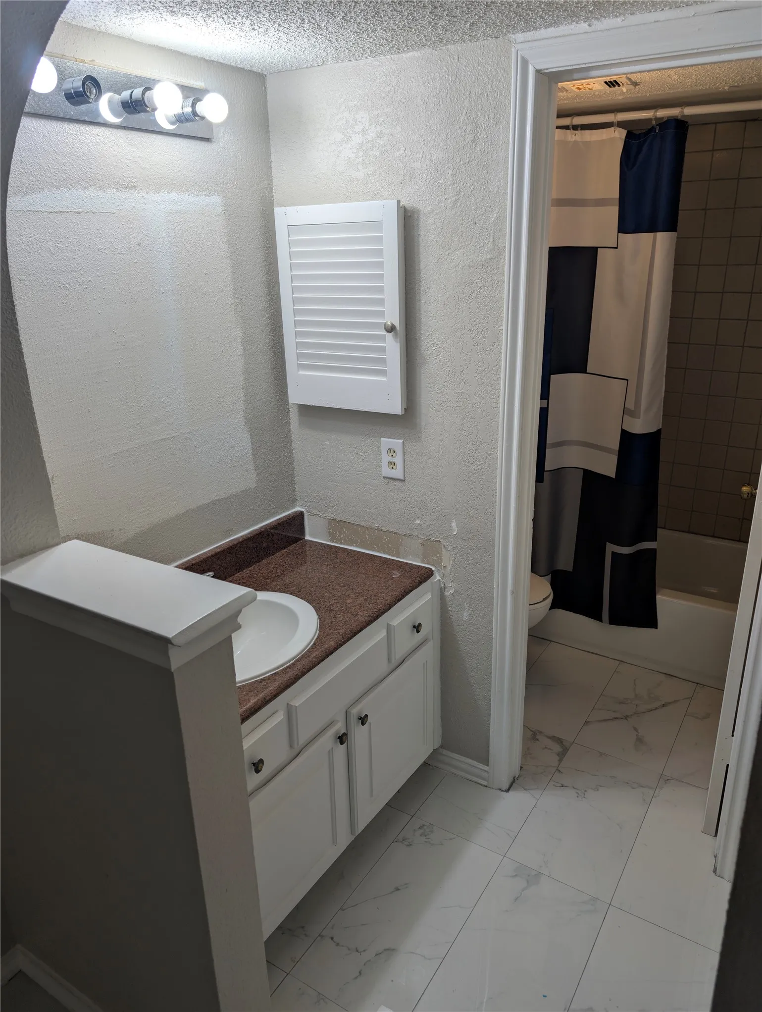 White vanity with integrated sink and contrasting countertop, white wall-mounted storage cabinet, and white tile flooring