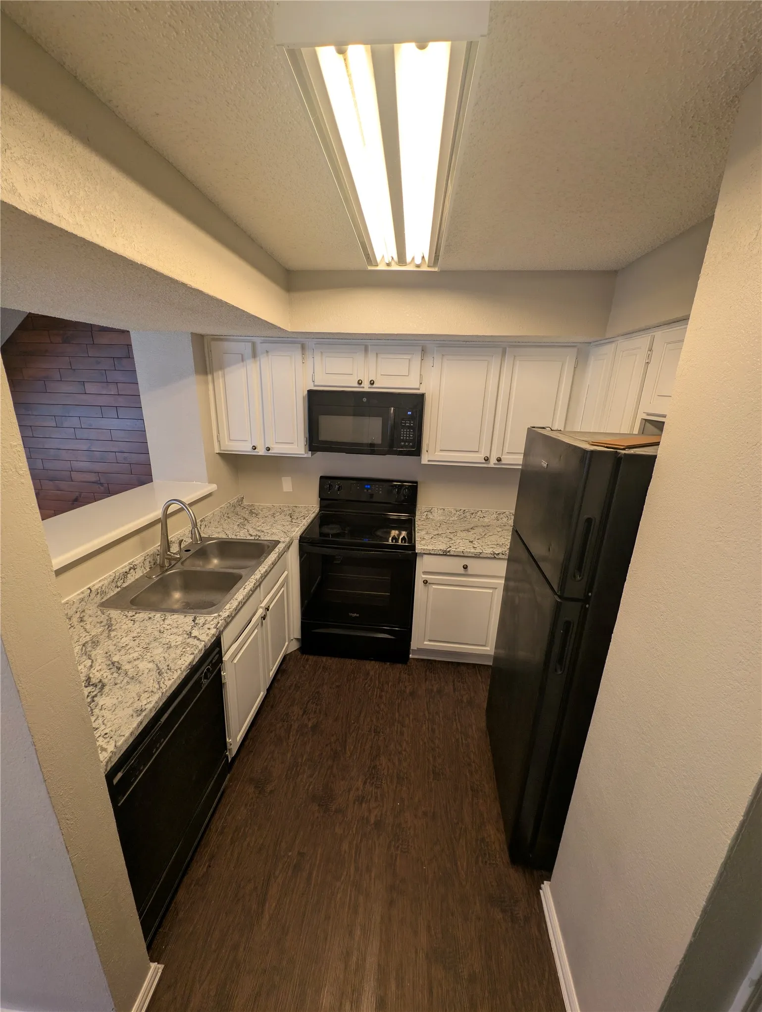 White cabinetry, wood-finish flooring, undermount double-basin sink with a gooseneck faucet, black appliances, and light-toned countertops