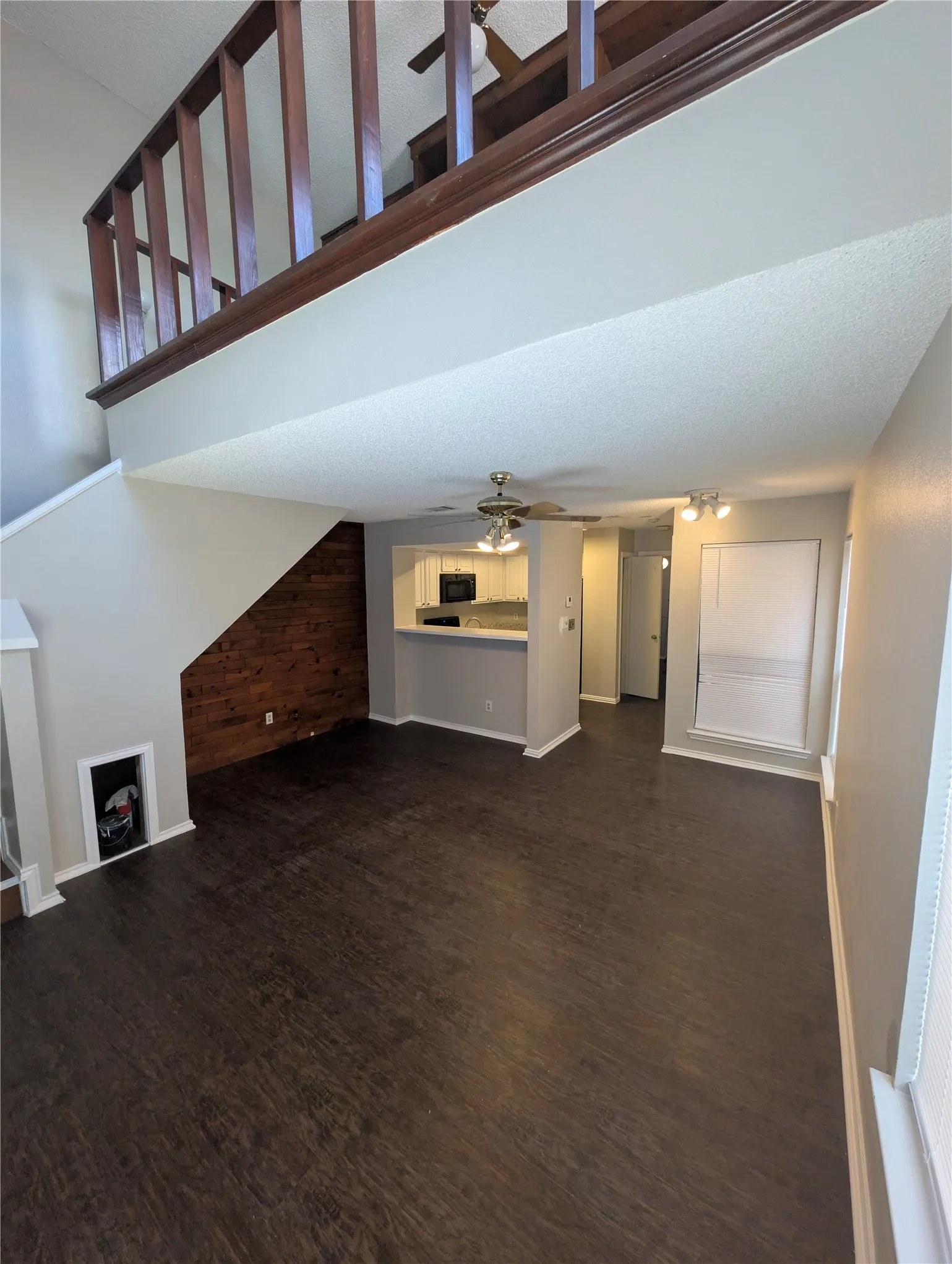 Open-concept living area with dark wood-finish flooring, a wood accent wall, and a ceiling fan