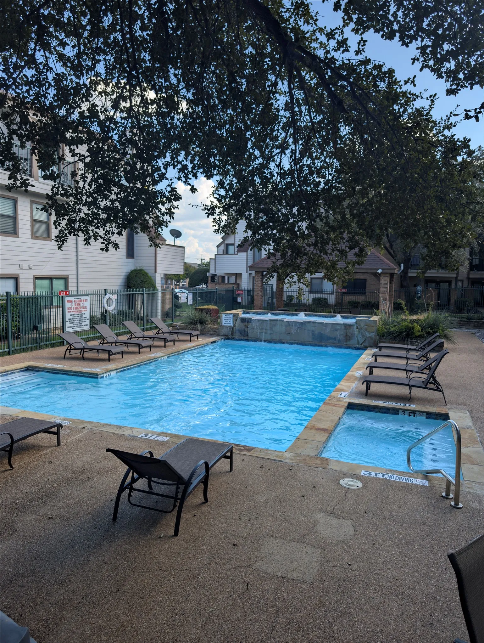 Swimming pool with integrated spa and waterfall feature, surrounded by a concrete deck with stone coping