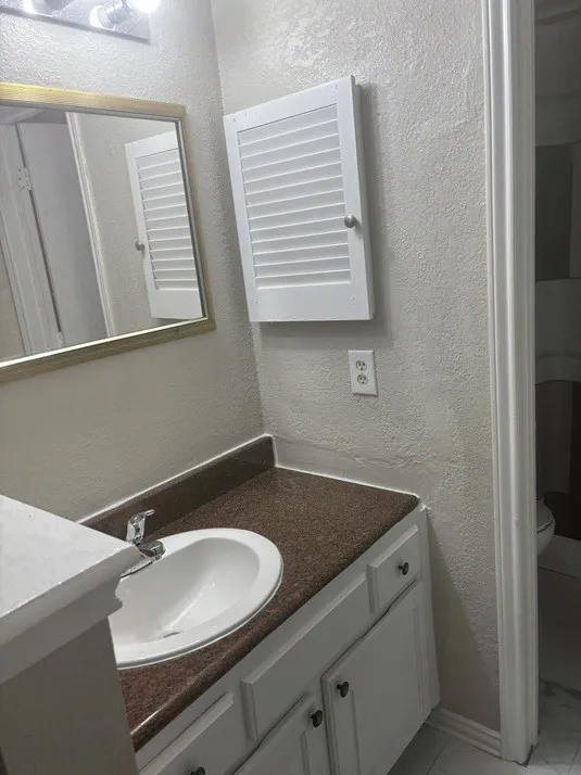 White vanity with integrated sink, brown speckled countertop, and wall-mounted storage cabinet