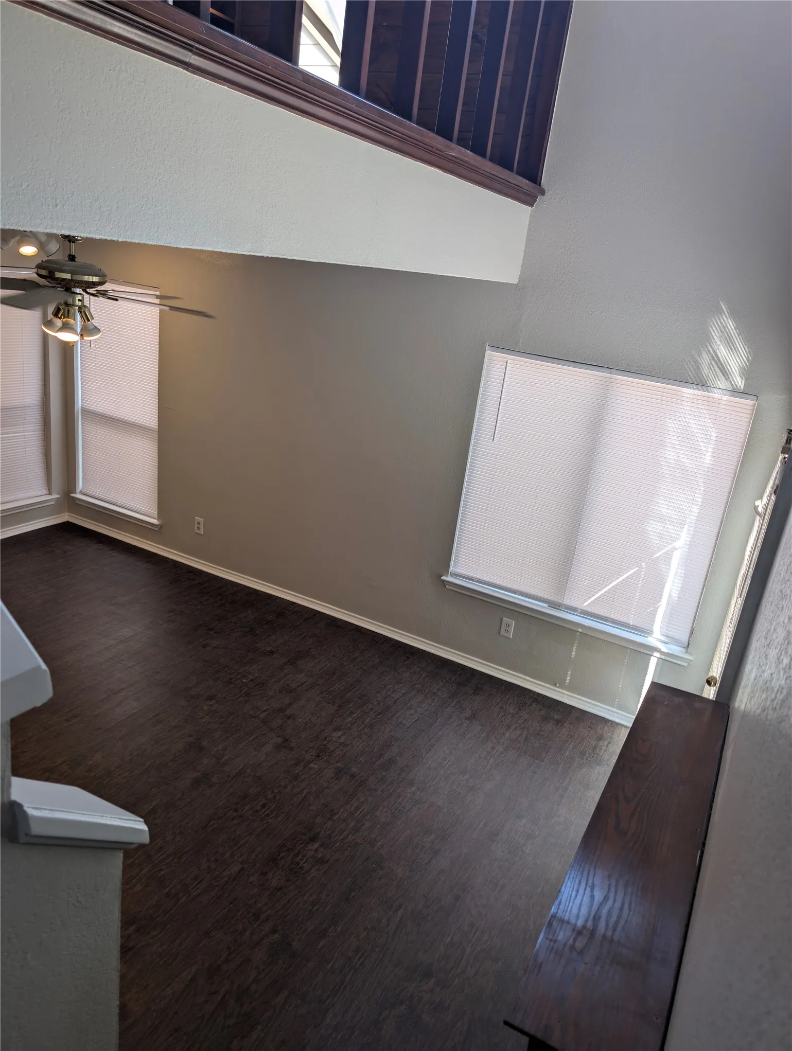 Open-concept living area with dark wood-finish flooring, multiple windows providing natural light, and a ceiling fan with integrated lighting
