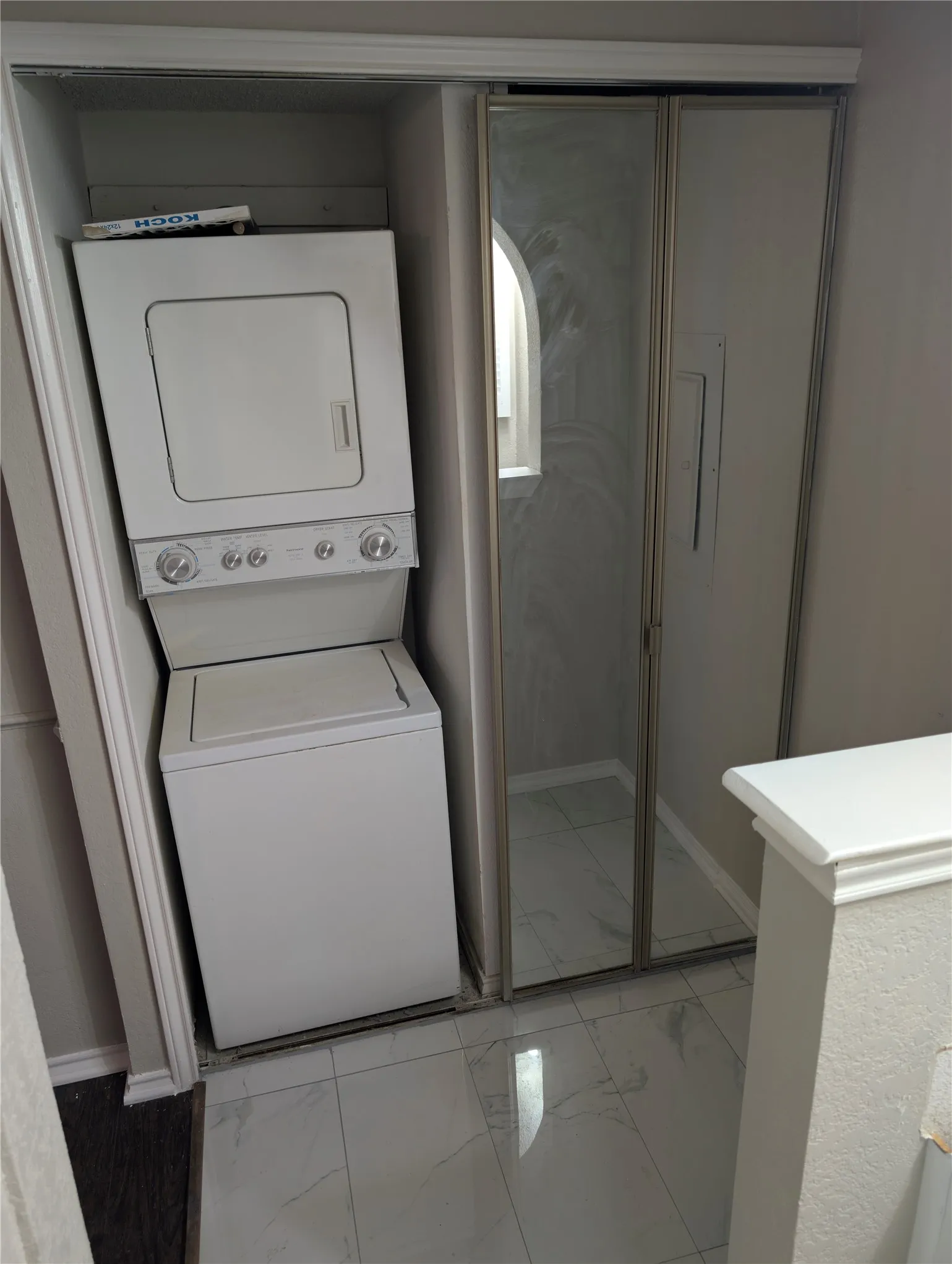 Stacked laundry appliances, white tile flooring, and mirrored closet doors
