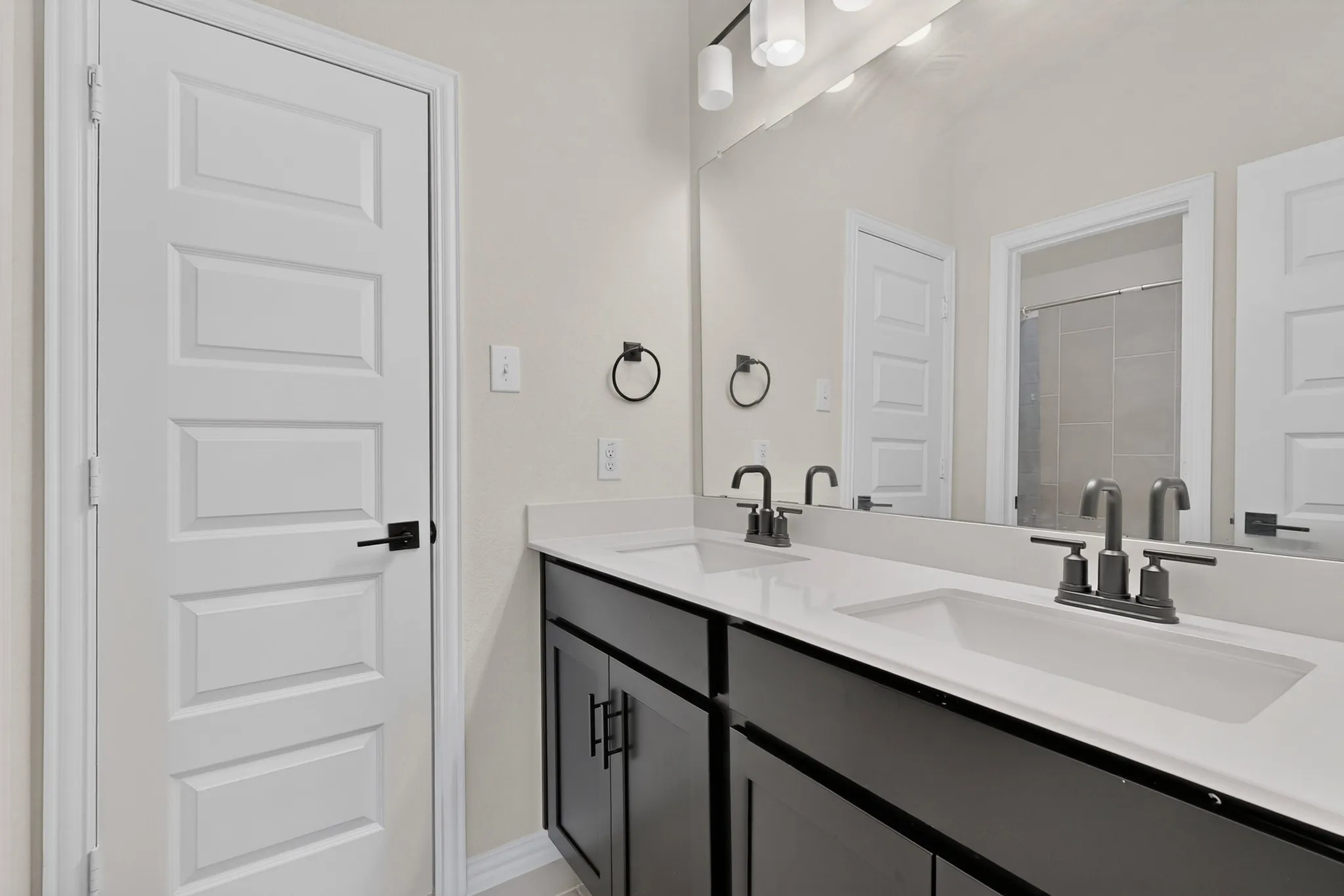 Dual vanity with dark cabinetry, white countertops, integrated sinks, and dark-finish faucets