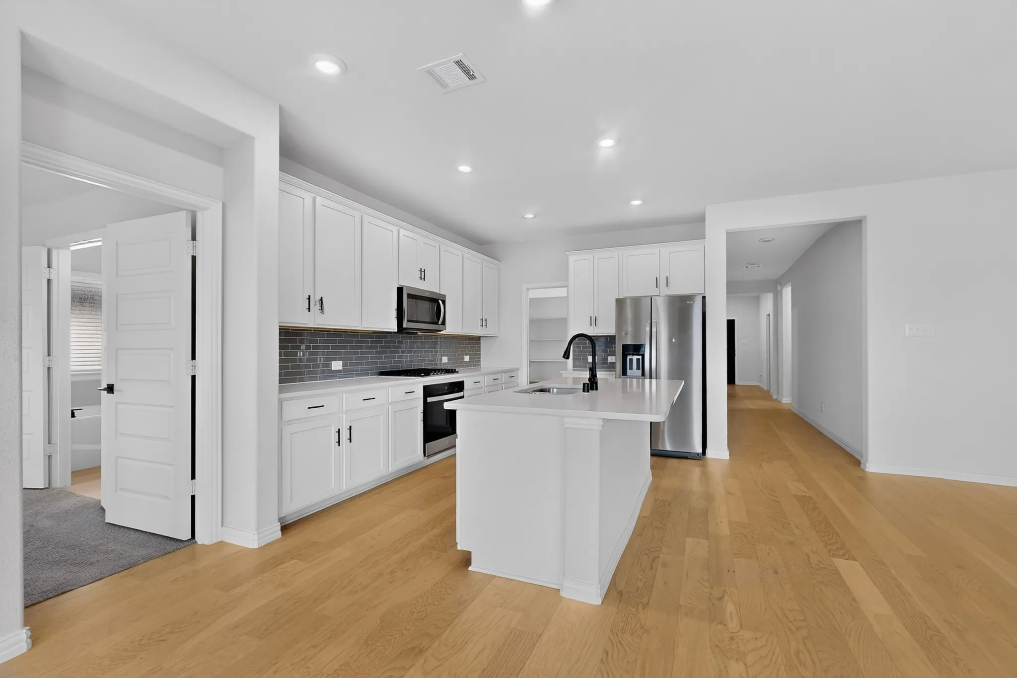 Open-concept kitchen with light wood-finish flooring, white cabinetry, a center island with a sink, and stainless steel appliances