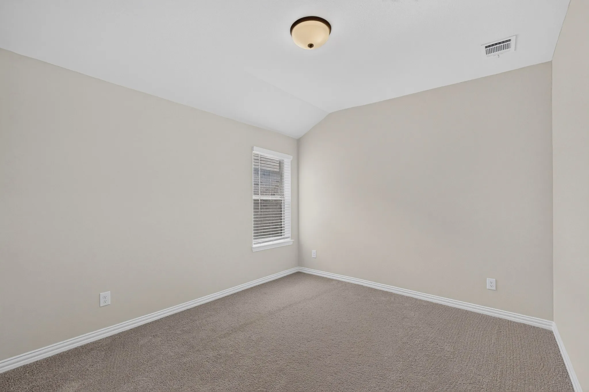 Carpeted flooring, vaulted ceiling, neutral wall paint, window with blinds, and a flush-mount ceiling light
