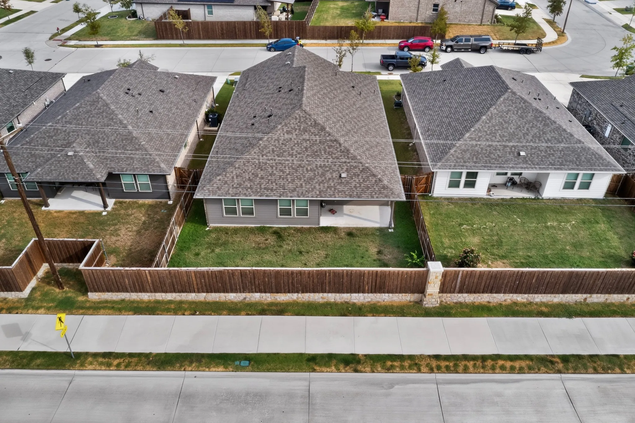 Gabled roof architecture, rear patio, fenced backyard, concrete sidewalk, and street frontage