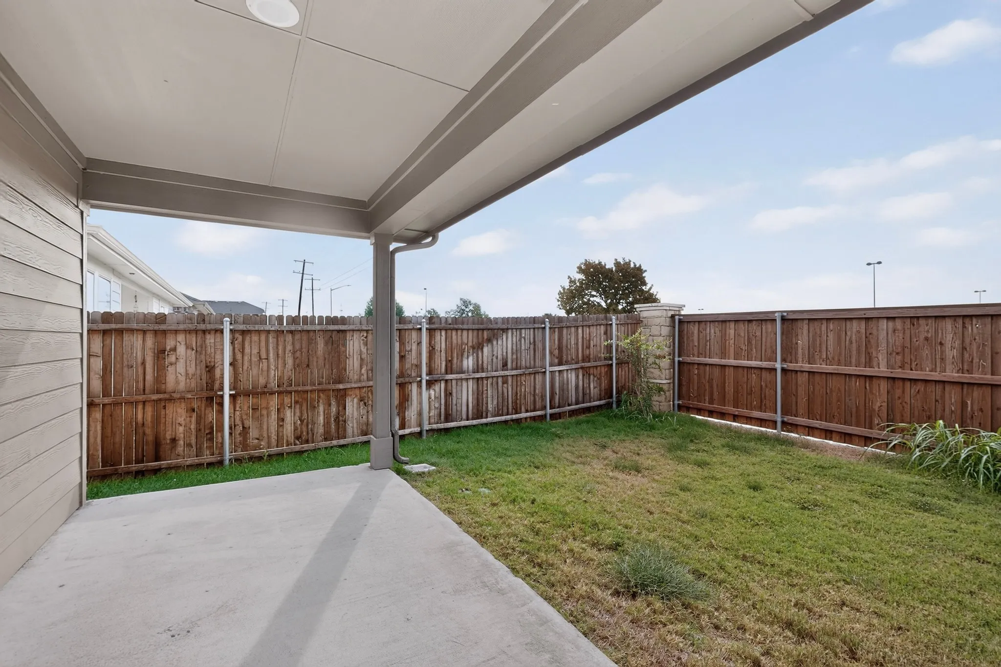 Covered concrete patio with recessed lighting, bordered by a wood privacy fence and a grassy yard