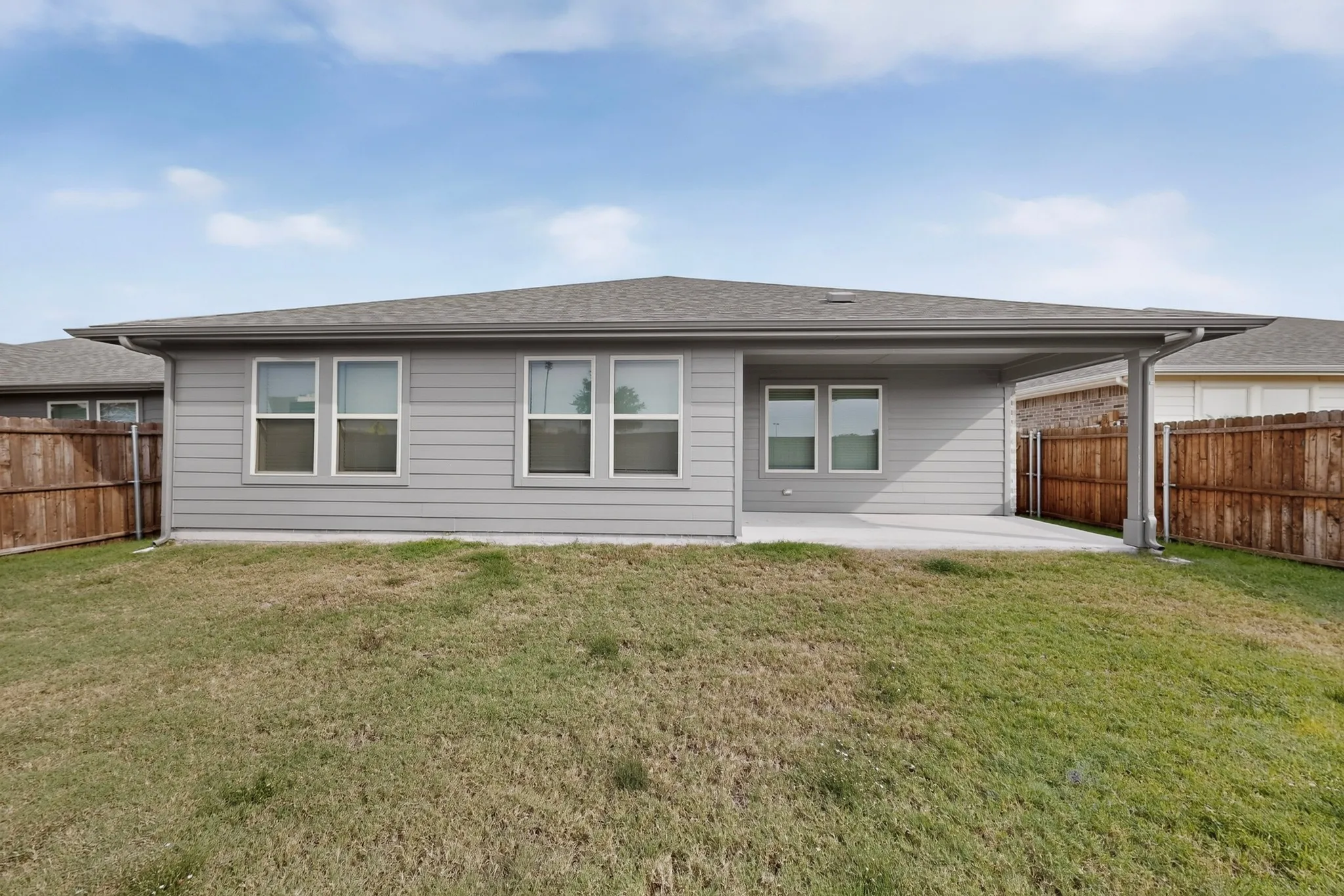 Expansive backyard featuring a covered patio, gray siding, multiple windows, and a wood privacy fence