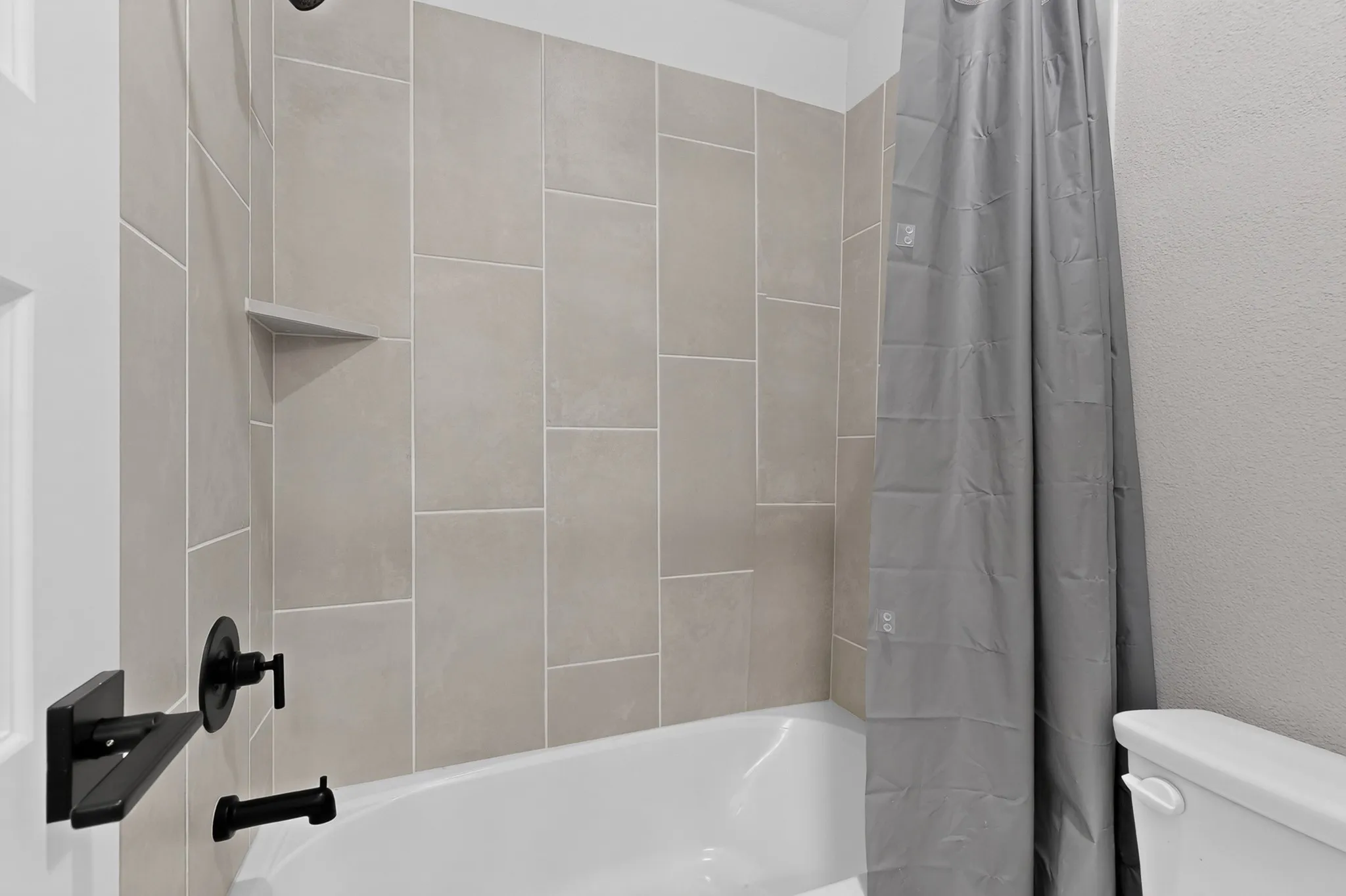 Bathtub with light-toned wall tiling, built-in corner shelf, and matte black fixtures